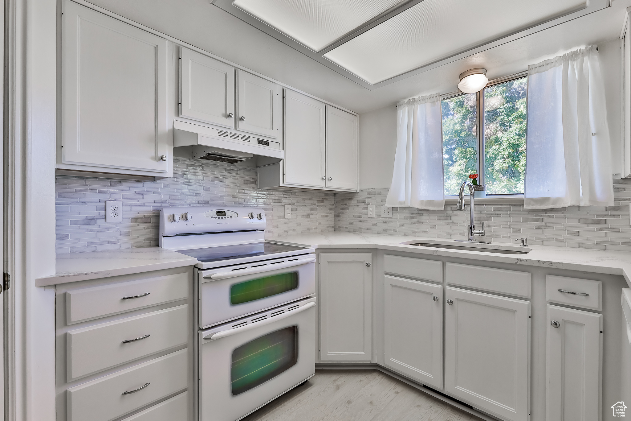 Kitchen with quartz counters, range hood, sink, white cabinets, and range with double oven oven