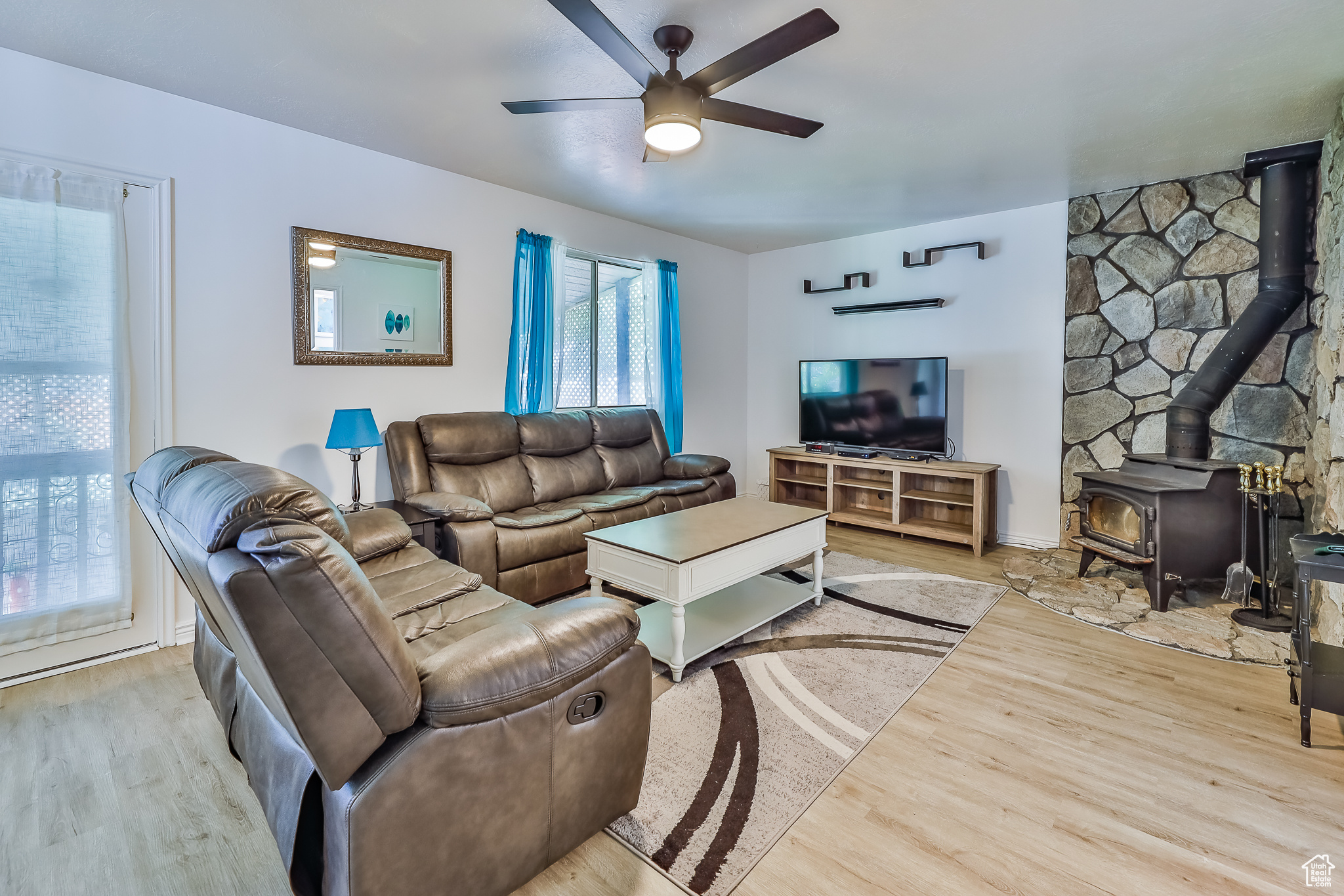 Living room featuring ceiling fan, light wood-type flooring, and a wood stove