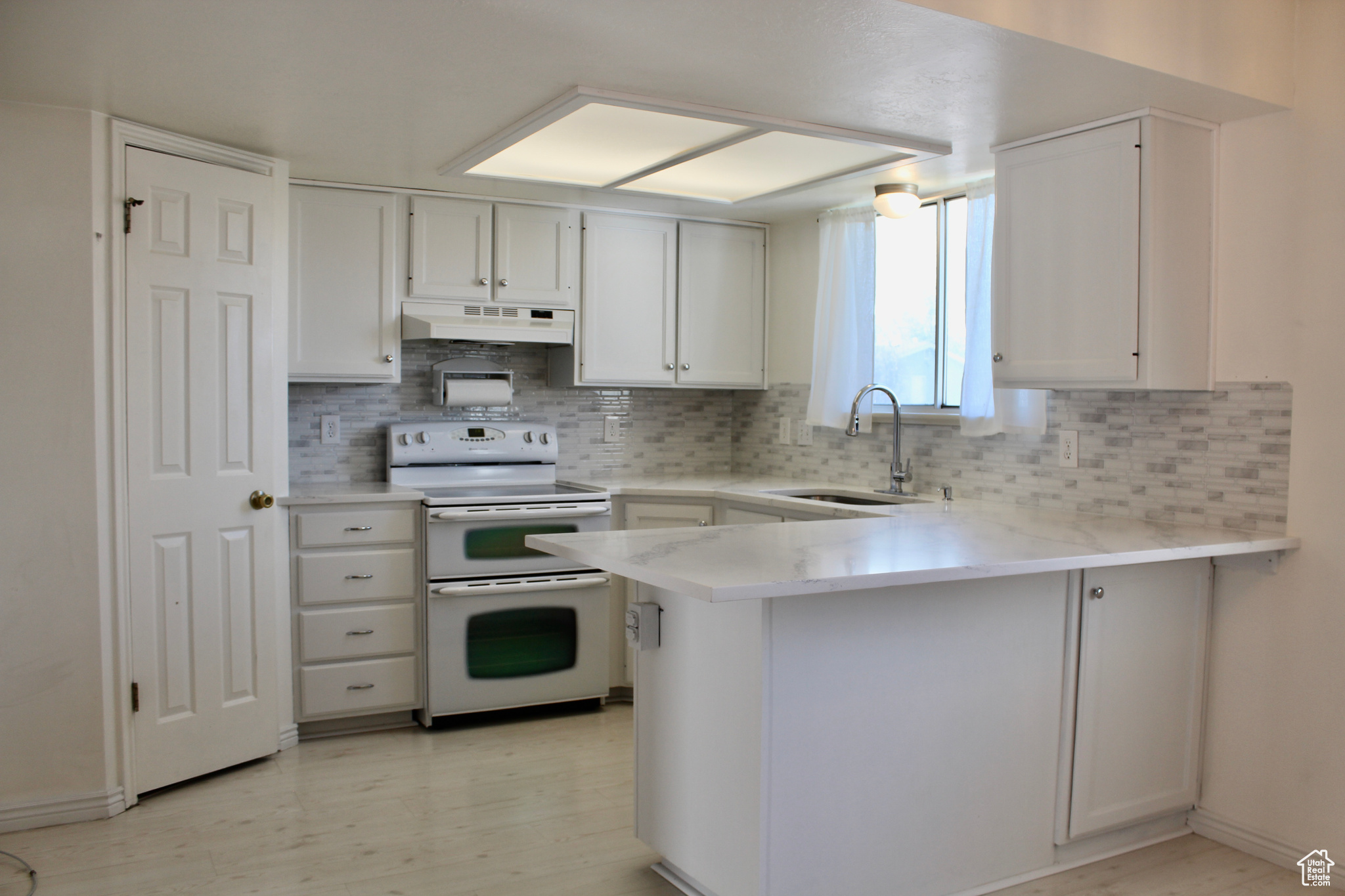 Kitchen with quartz counters, range hood, sink, white cabinets, and range with double oven oven