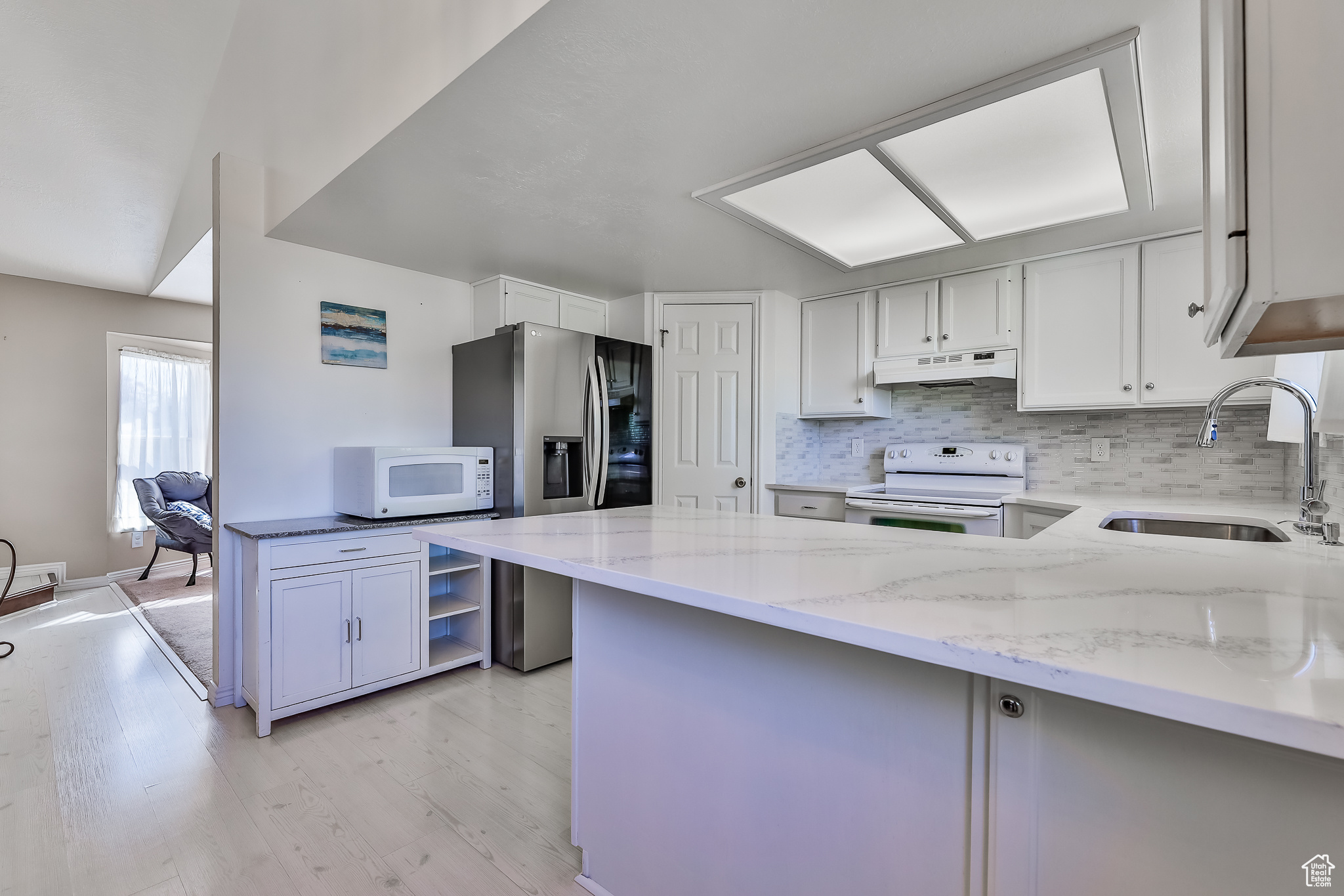 Kitchen with quartz counters, range hood, sink, white cabinets, and range with double oven oven