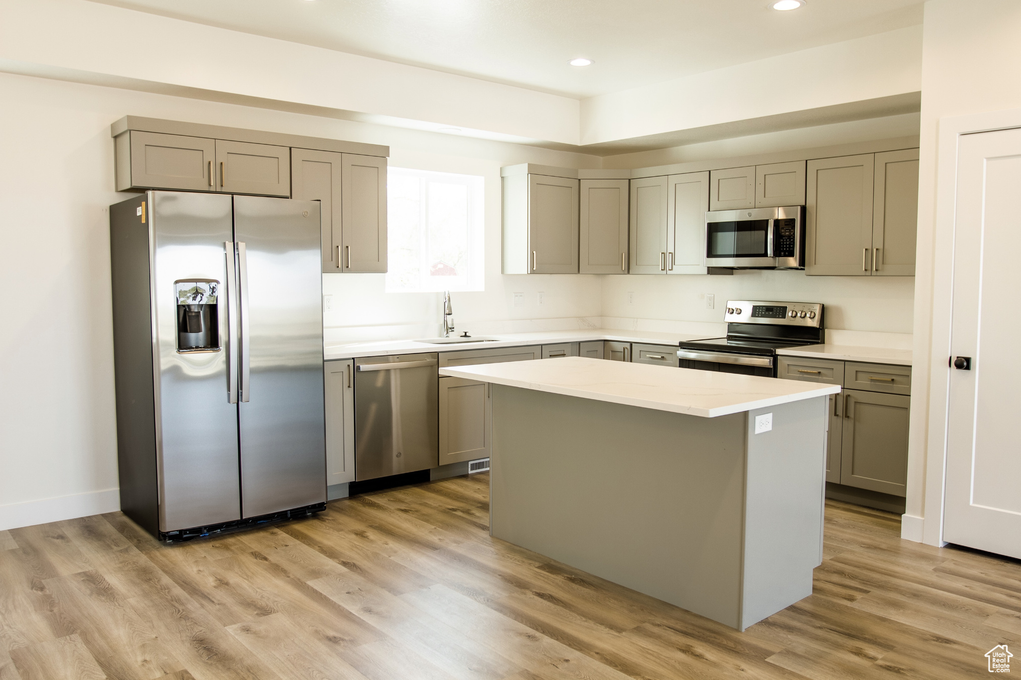 Kitchen with a center island, LVP flooring, gray cabinetry, stainless steel appliances, and sink