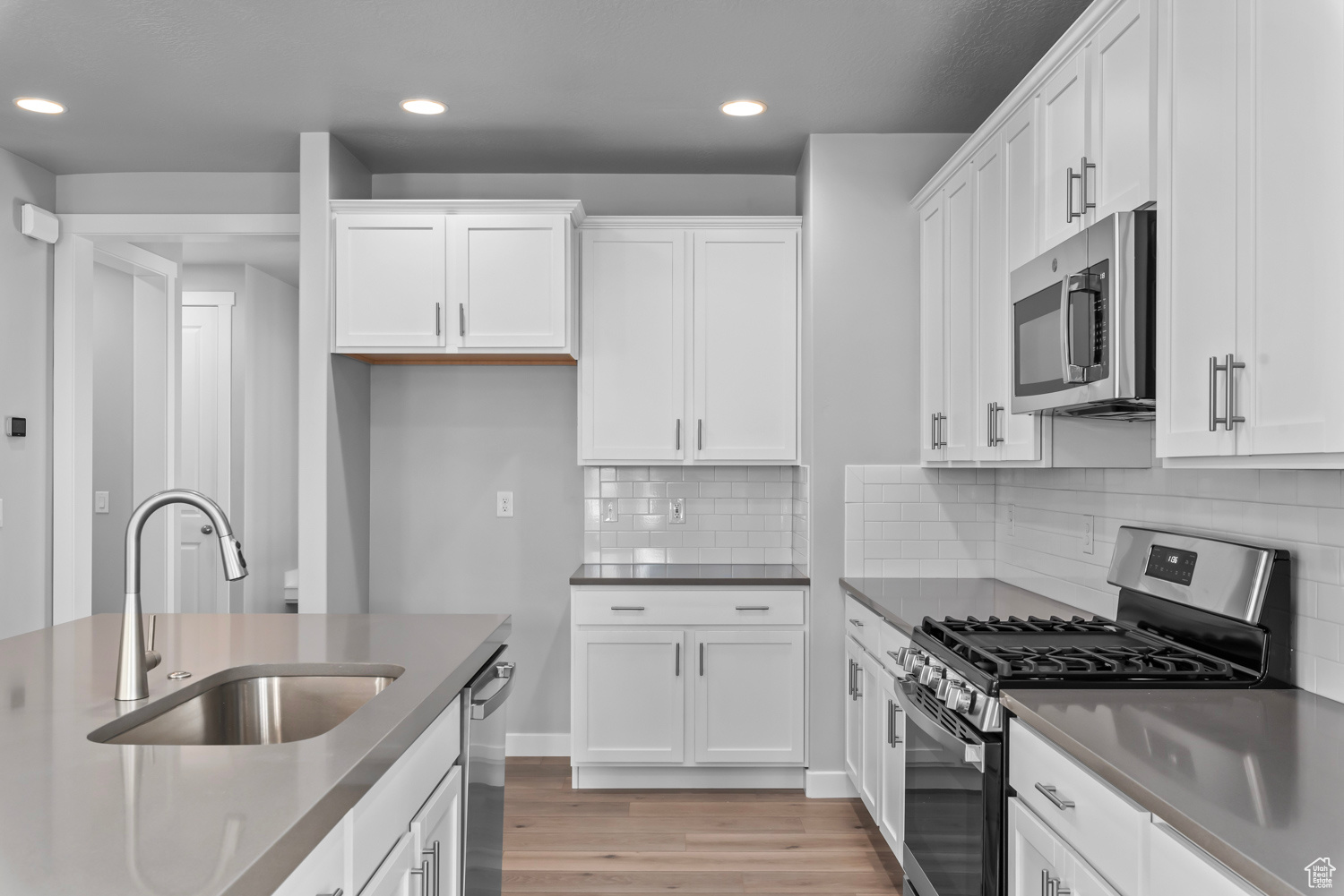 Kitchen featuring white cabinets, stainless steel appliances, backsplash, light wood-type flooring, and sink