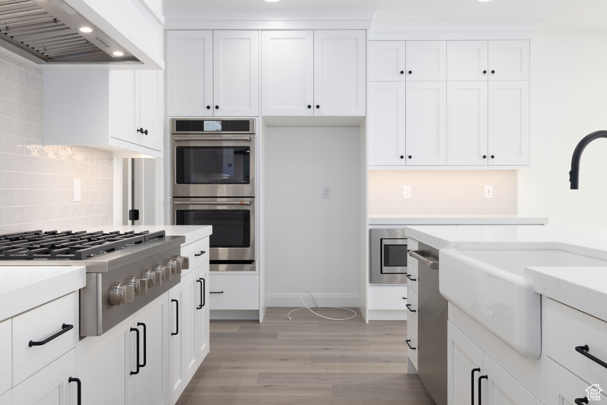 Kitchen with appliances with stainless steel finishes, tasteful backsplash, premium range hood, and light hardwood / wood-style flooring