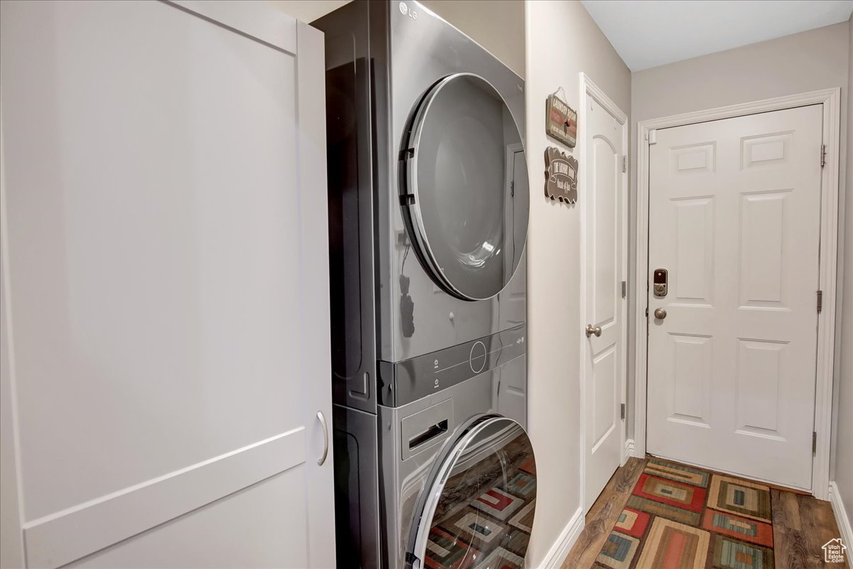 Clothes washing area featuring dark wood-type flooring and stacked washer and clothes dryer