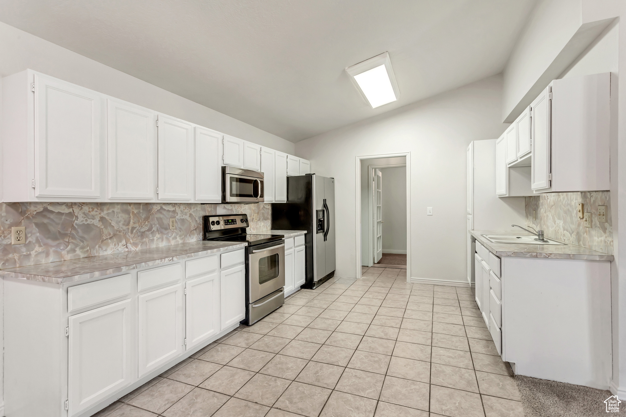 Spacious kitchen featuring white cabinets with lots of counter space and stainless steel appliances