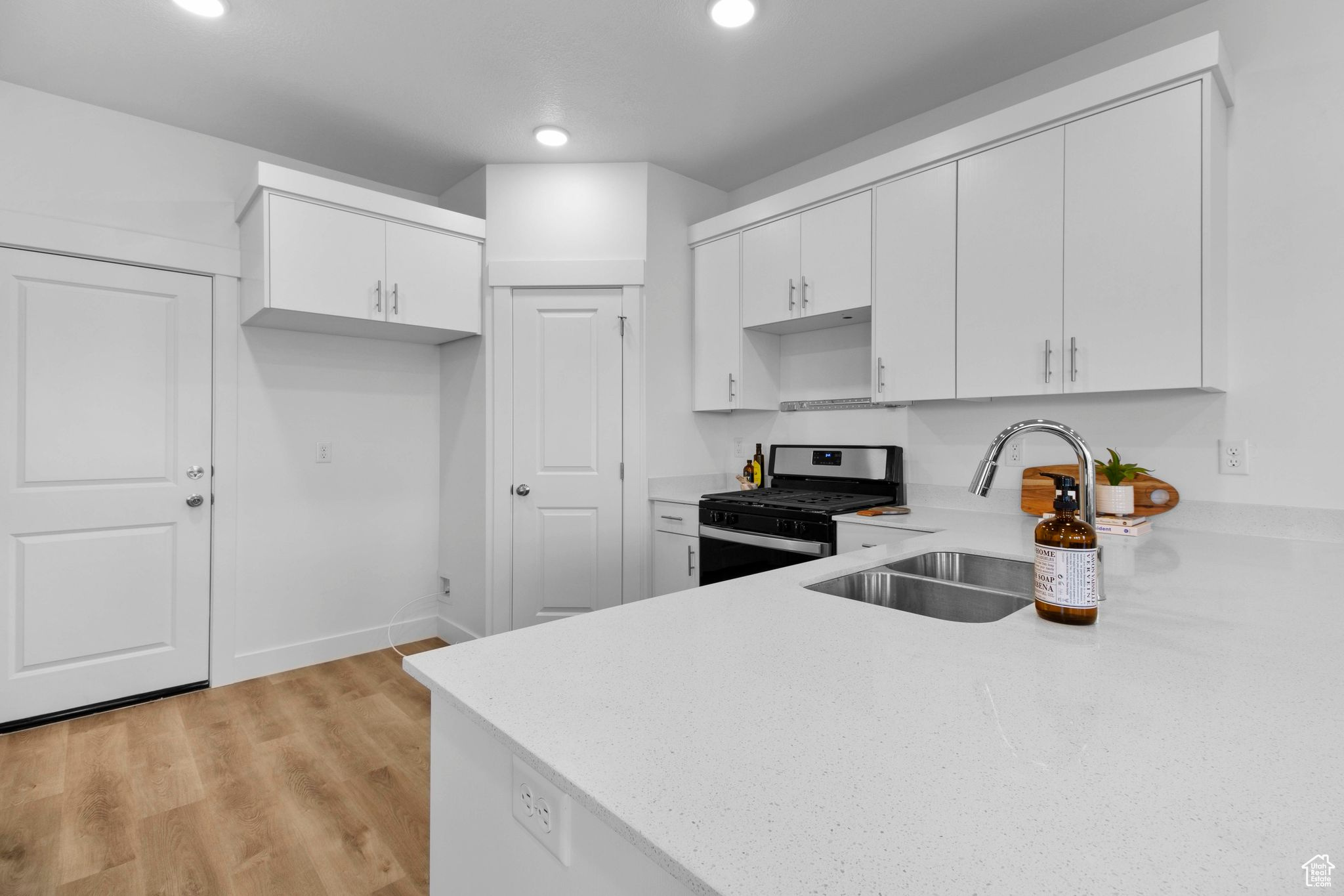 Kitchen featuring light hardwood / wood-style flooring, sink, white cabinetry, and stainless steel gas range oven