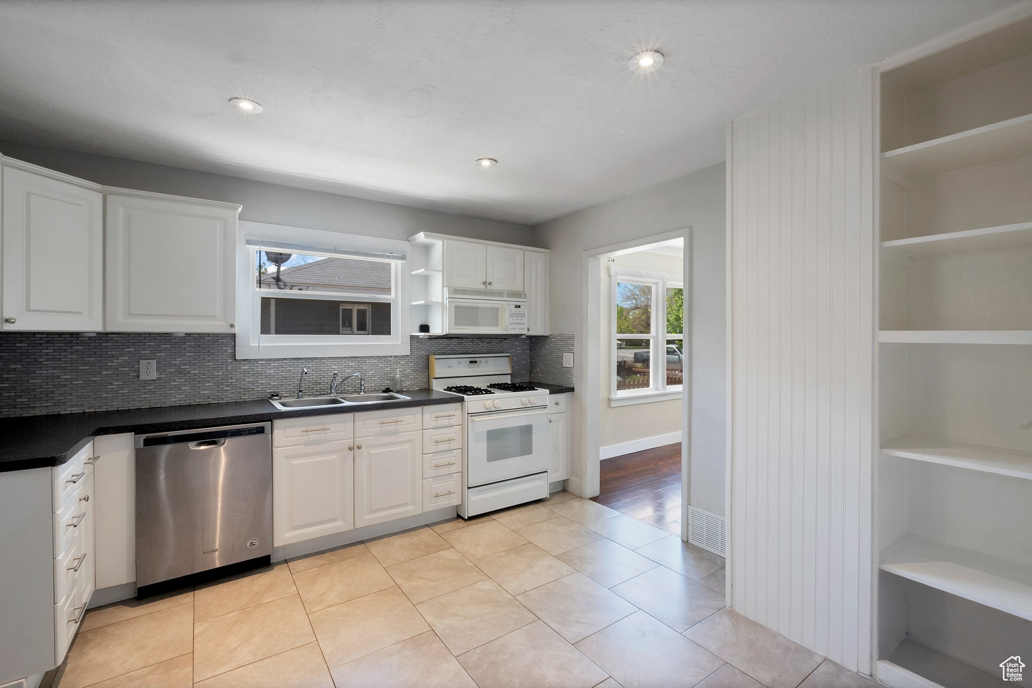 Kitchen with tasteful backsplash, white appliances, light tile flooring, sink, and white cabinets