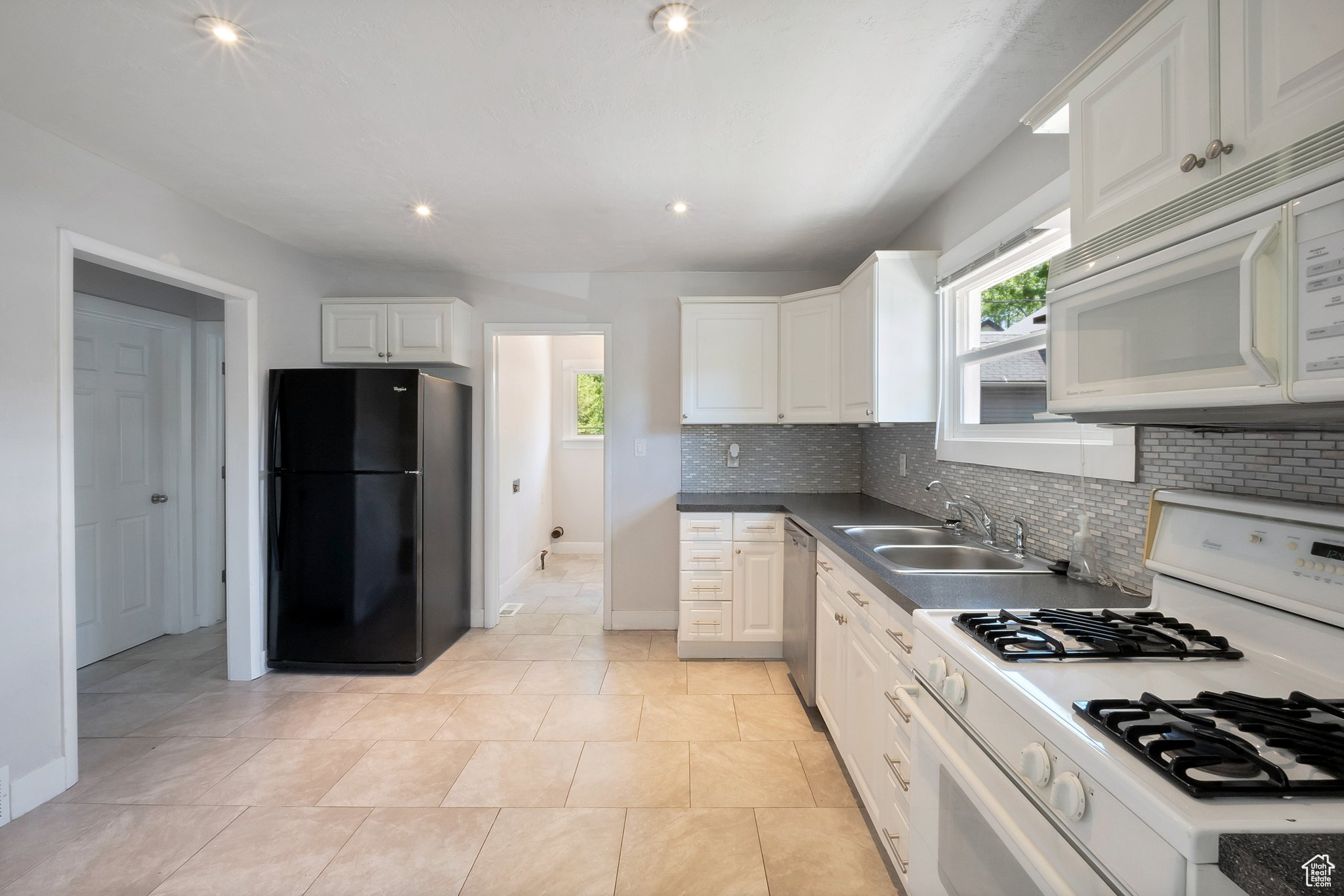 Kitchen featuring white cabinets, light tile flooring, backsplash, sink, and white appliances