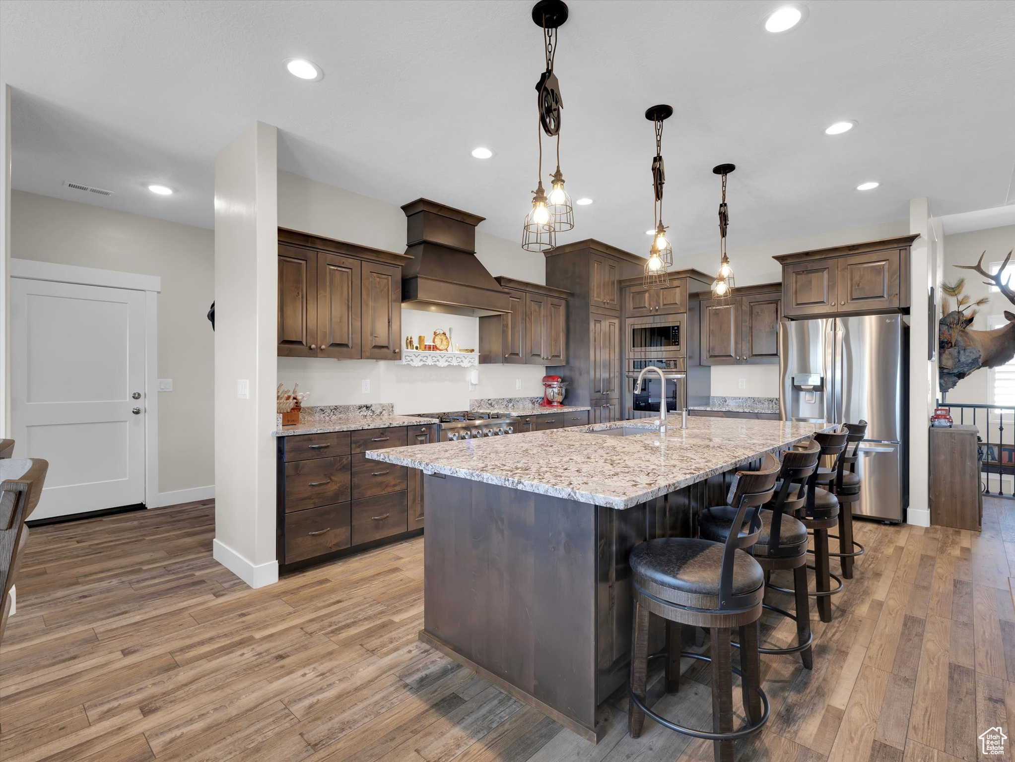 Kitchen featuring premium range hood, light hardwood / wood-style flooring, dark brown cabinets, gas range and stainless steel appliances