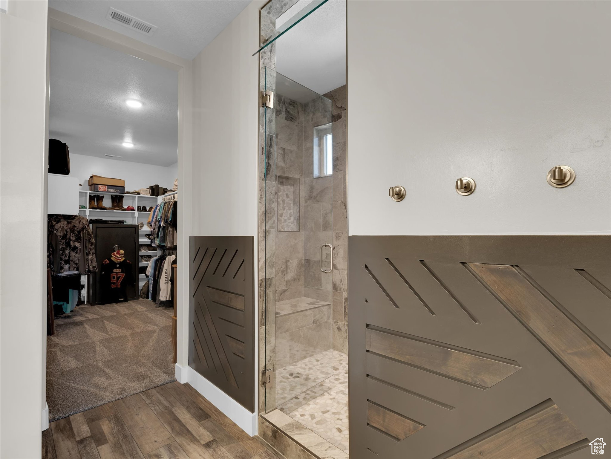 Primary bathroom with hardwood / wood-style flooring, wall feature and a tile shower