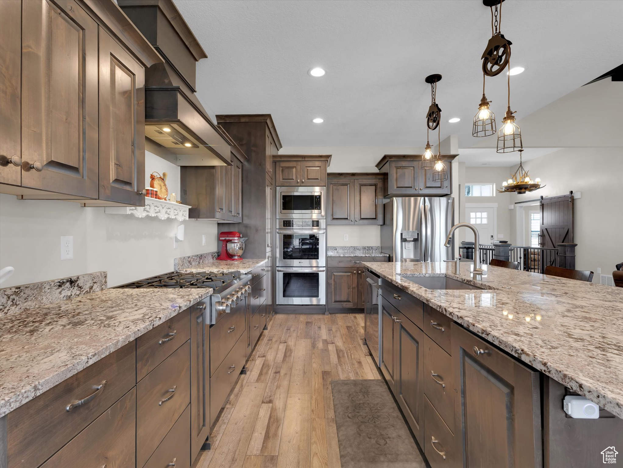 Kitchen featuring sink, decorative light fixtures, double ovens, dark brown cabinetry, and light wood-type flooring