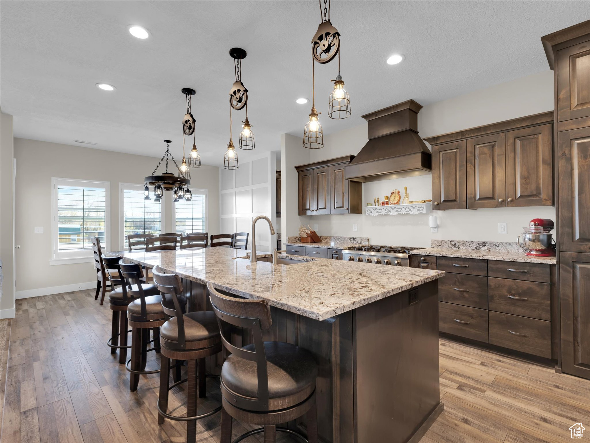 Kitchen featuring premium range hood, decorative light fixtures, gas range, light hardwood / wood-style floors, and an island with sink
