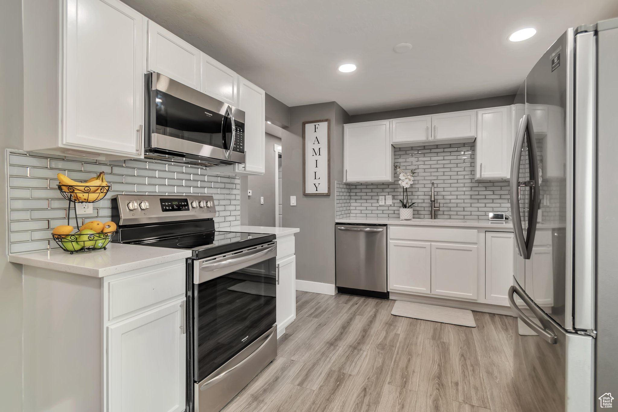Kitchen featuring sink, backsplash, light wood-type flooring, white cabinetry, and stainless steel appliances