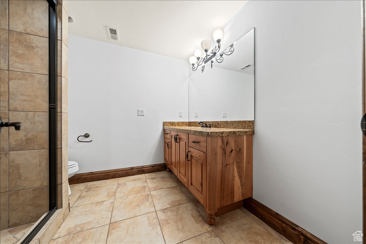 Bathroom with large vanity, a shower with shower door, toilet, and tile flooring