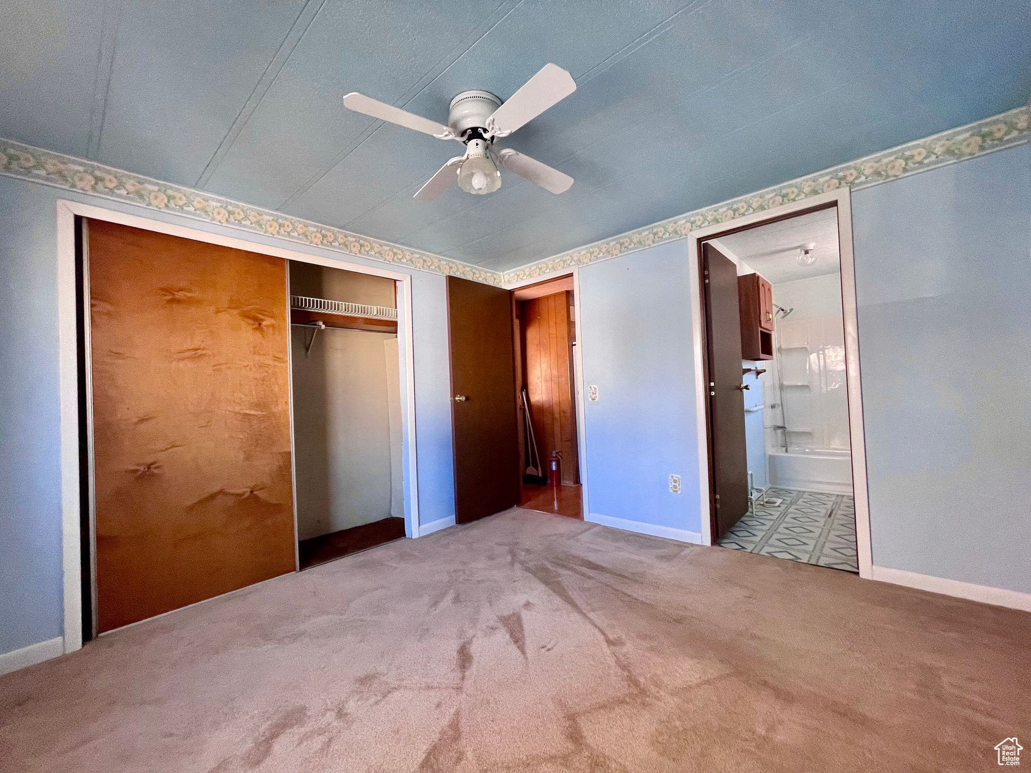 Unfurnished bedroom with light colored carpet, connected bathroom, ceiling fan, and a closet