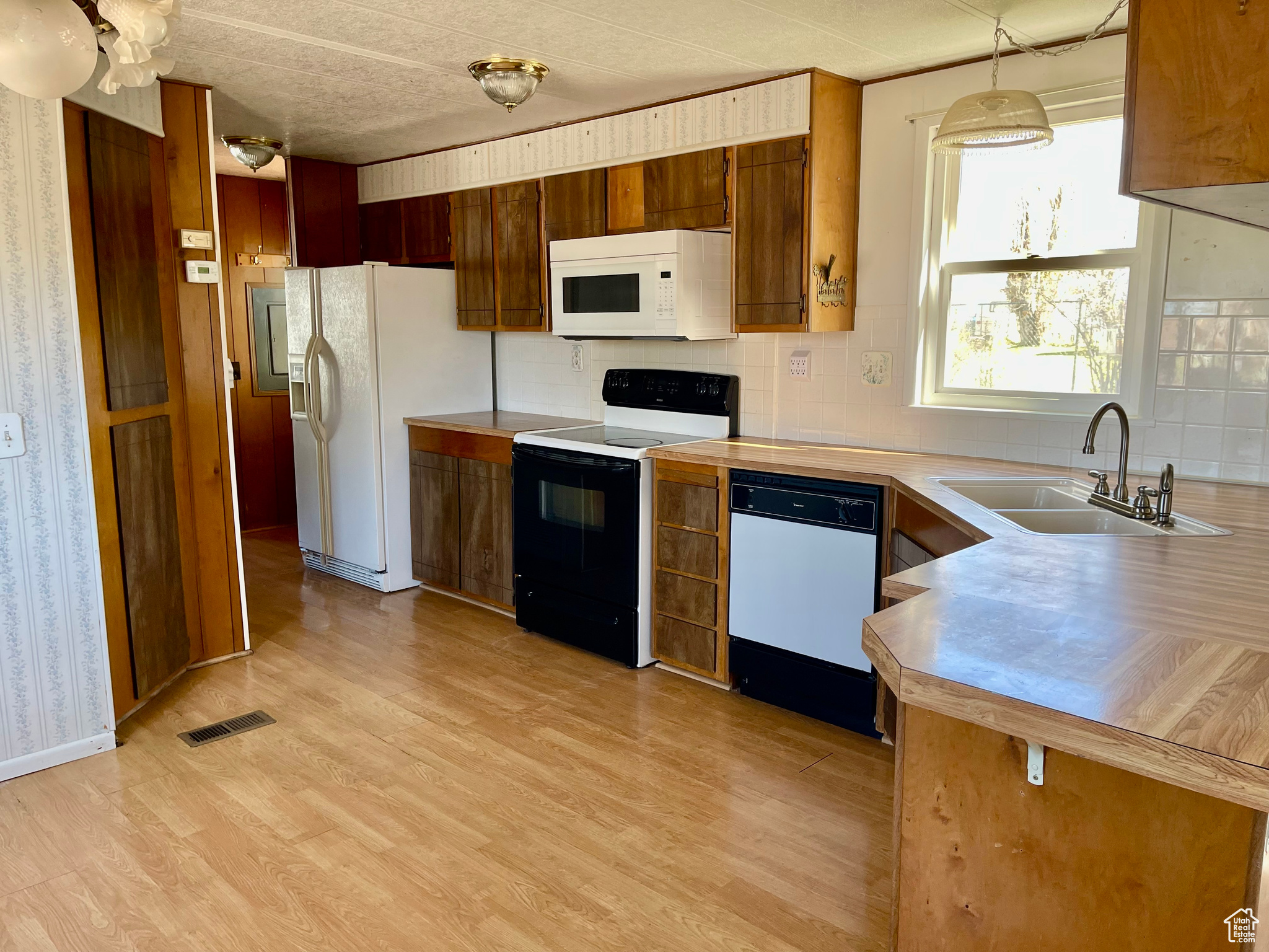 Kitchen featuring sink, white appliances, backsplash, decorative light fixtures, and light hardwood / wood-style flooring