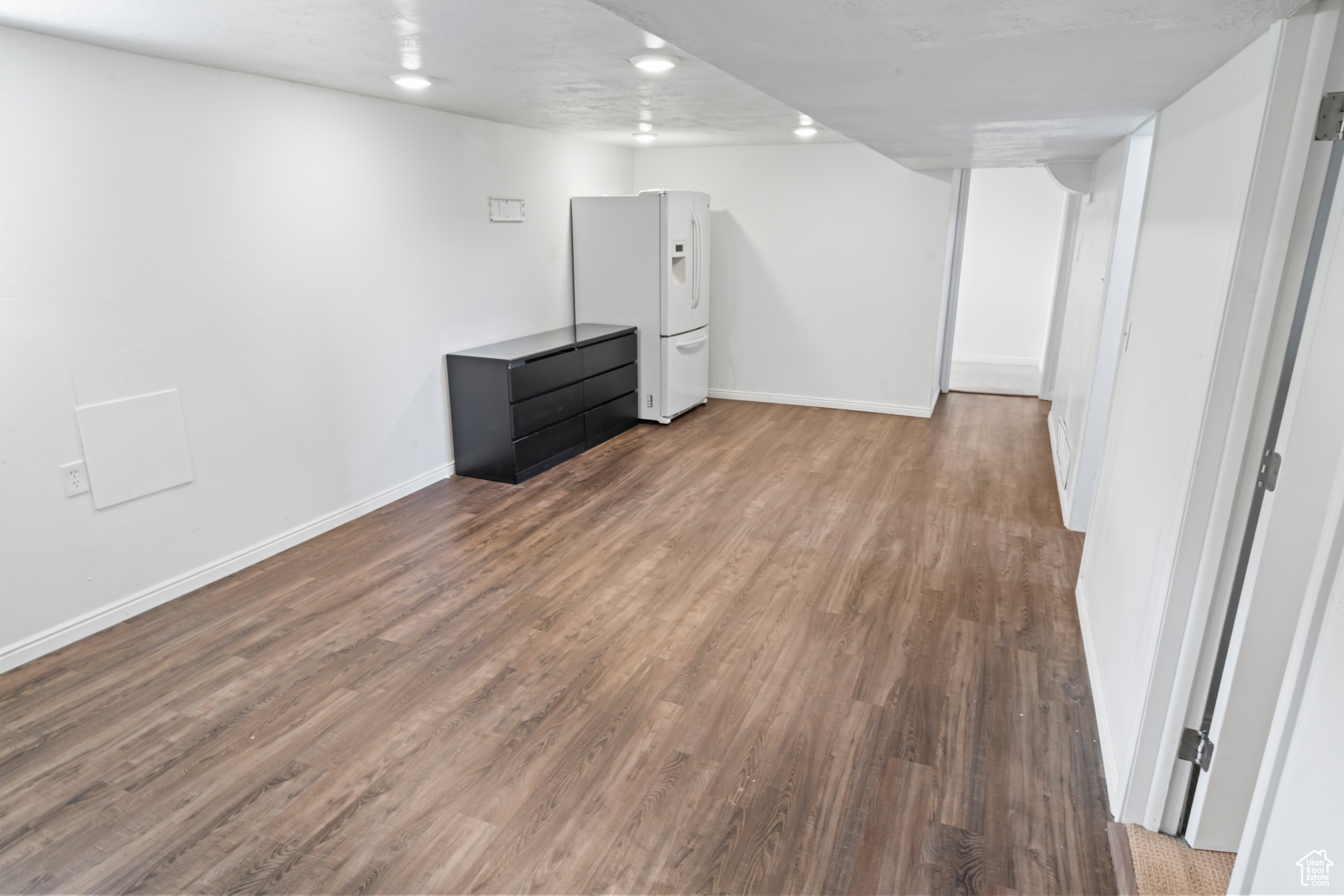 Basement featuring white fridge with ice dispenser and light wood-type flooring