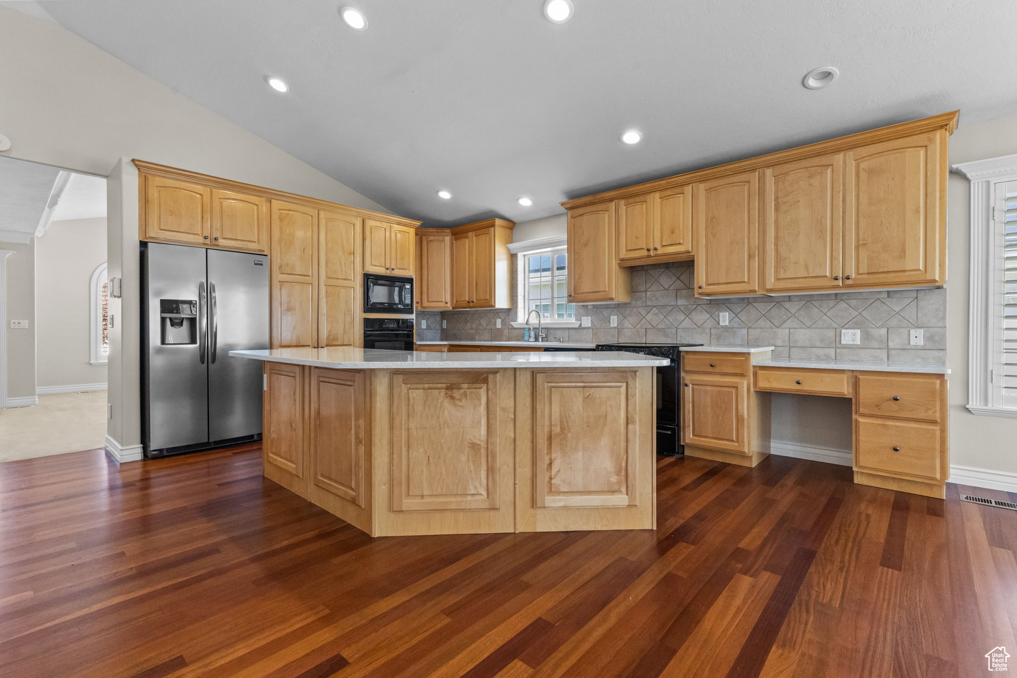 Kitchen featuring backsplash, stainless steel fridge with ice dispenser, a kitchen island, and dark wood-type flooring