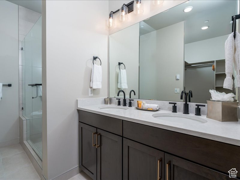 Bathroom with dual sinks, a shower with door, tile floors, and vanity with extensive cabinet space