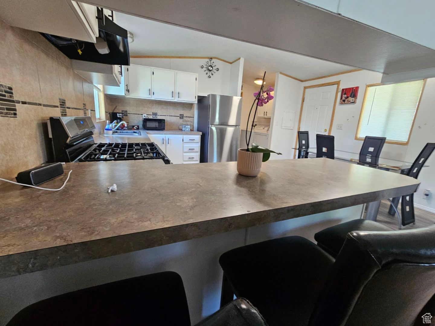 Kitchen featuring kitchen peninsula, stainless steel refrigerator, gas stove, backsplash, and white cabinetry