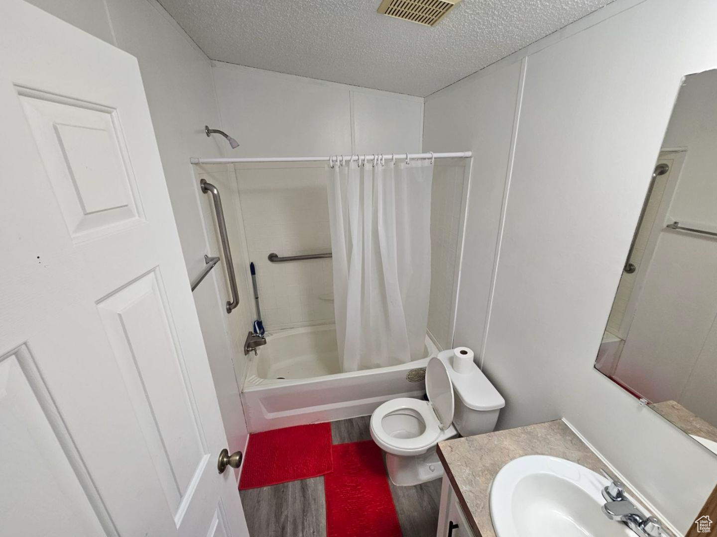 Full bathroom with vanity, toilet, a textured ceiling, and shower / bath combination with curtain