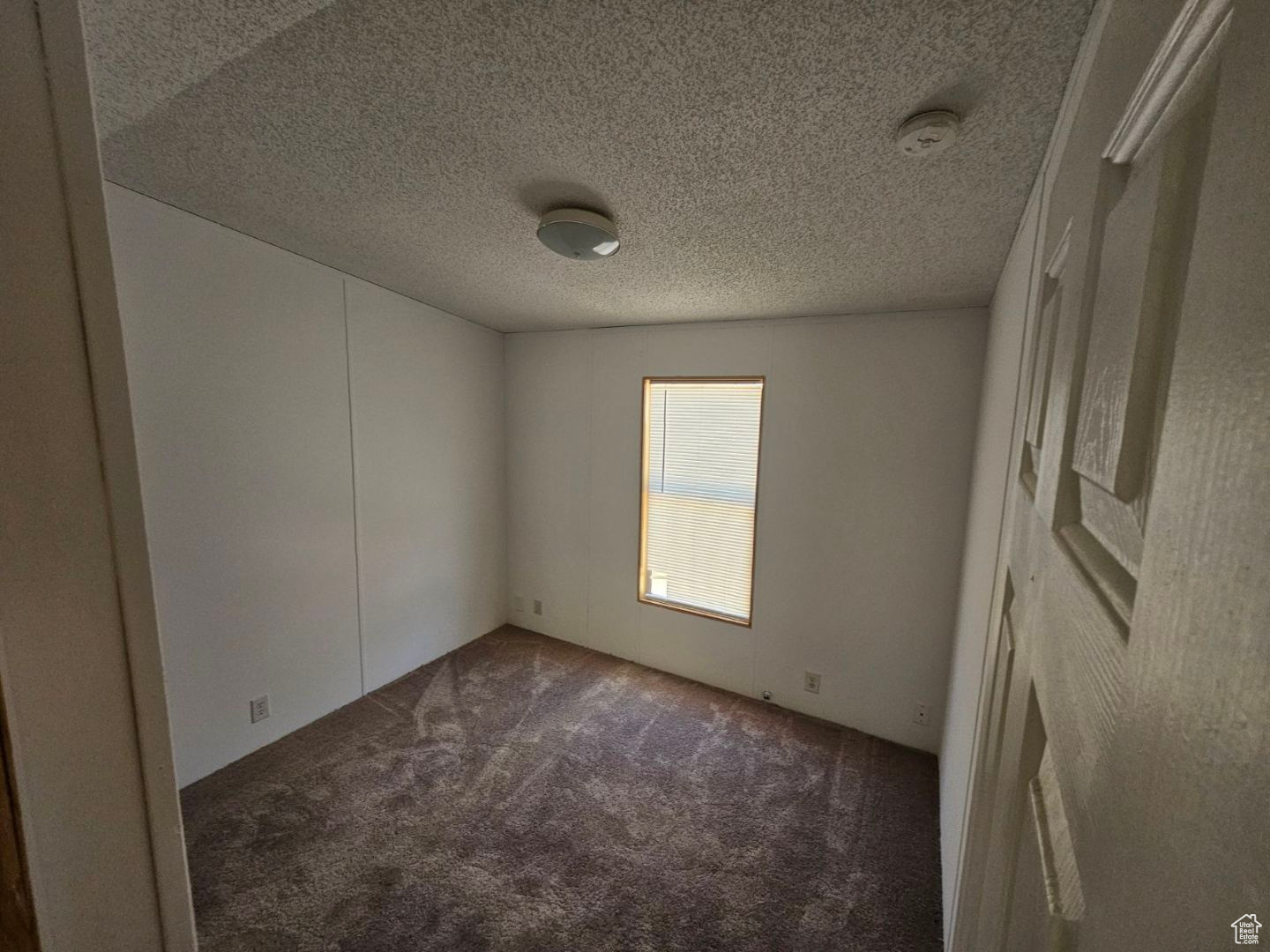 Spare room featuring dark colored carpet and a textured ceiling