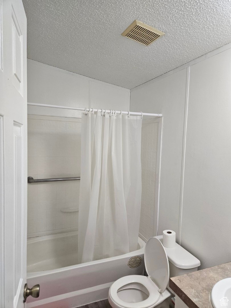 Full bathroom featuring vanity, a textured ceiling, toilet, and shower / tub combo with curtain