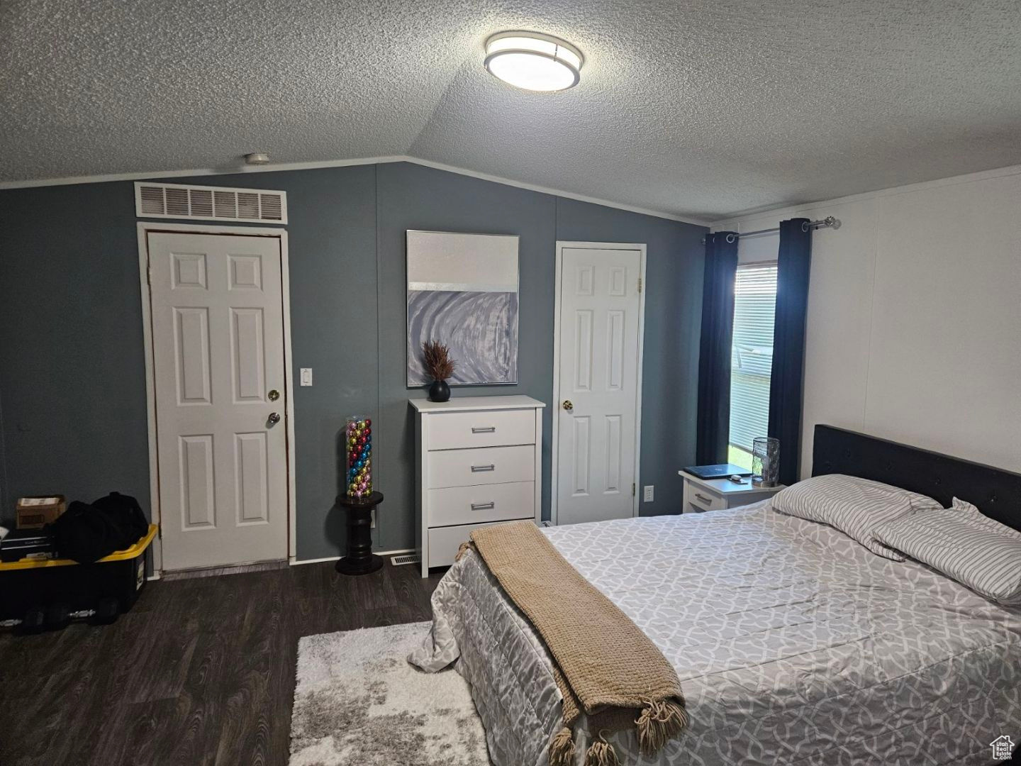 Bedroom with dark hardwood / wood-style floors, vaulted ceiling, and a textured ceiling