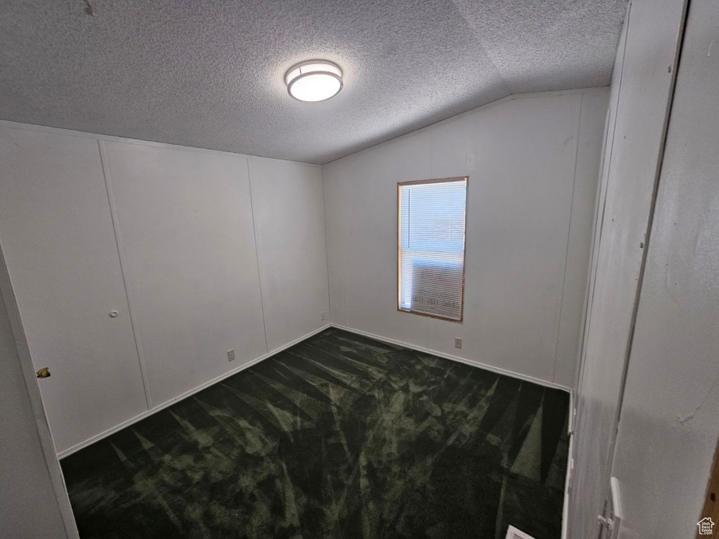 Carpeted spare room featuring a textured ceiling and vaulted ceiling