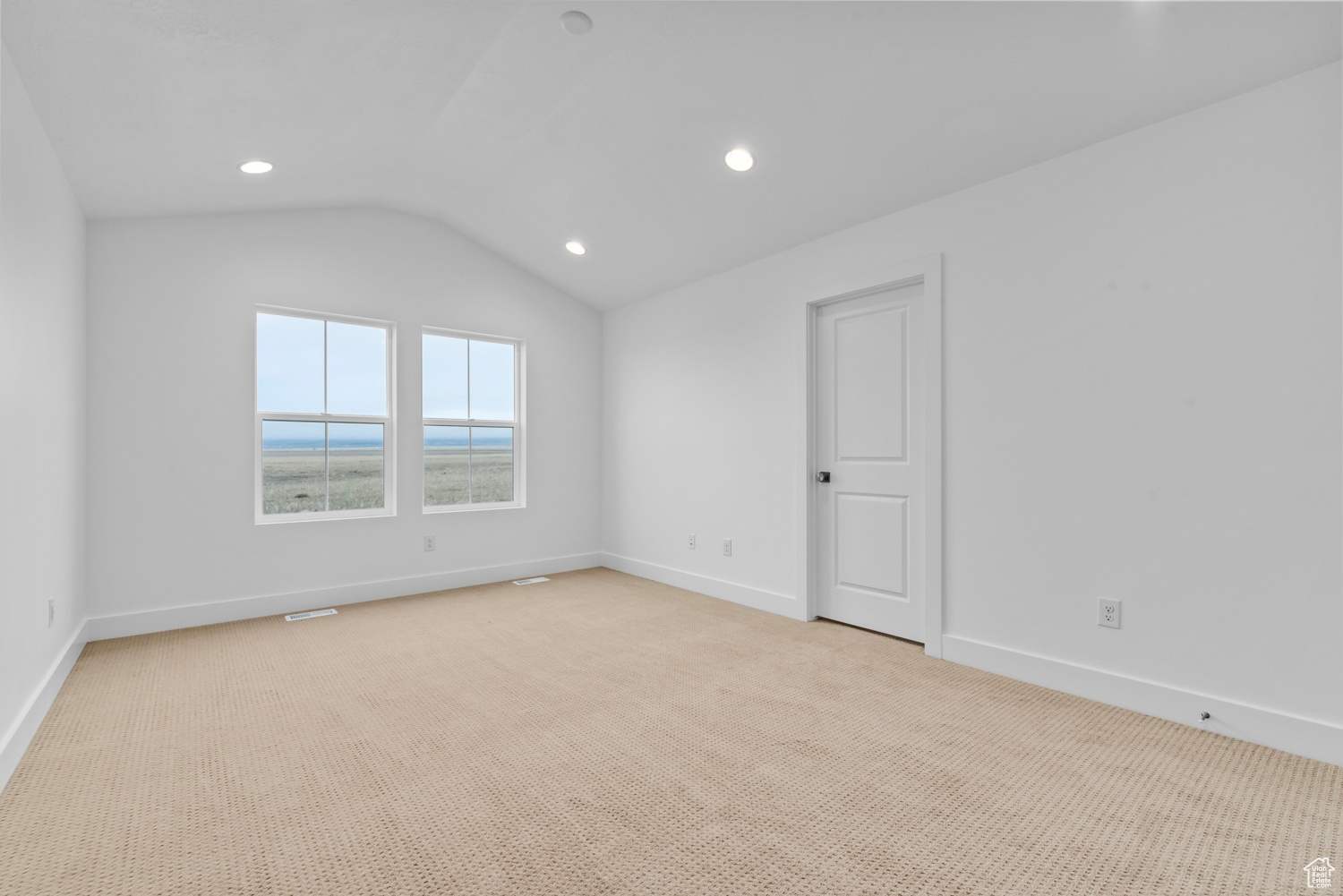 Empty room featuring light colored carpet and vaulted ceiling