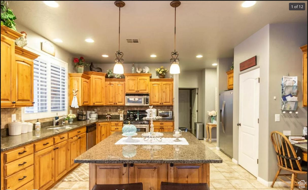 Kitchen featuring a kitchen island, stainless steel appliances, light tile floors, and hanging light fixtures