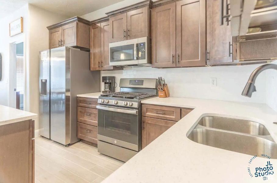 Kitchen with sink, tasteful backsplash, light wood-type flooring, and stainless steel appliances