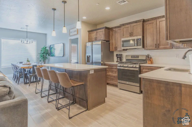 Kitchen with appliances with stainless steel finishes, sink, decorative light fixtures, light hardwood / wood-style flooring, and an inviting chandelier