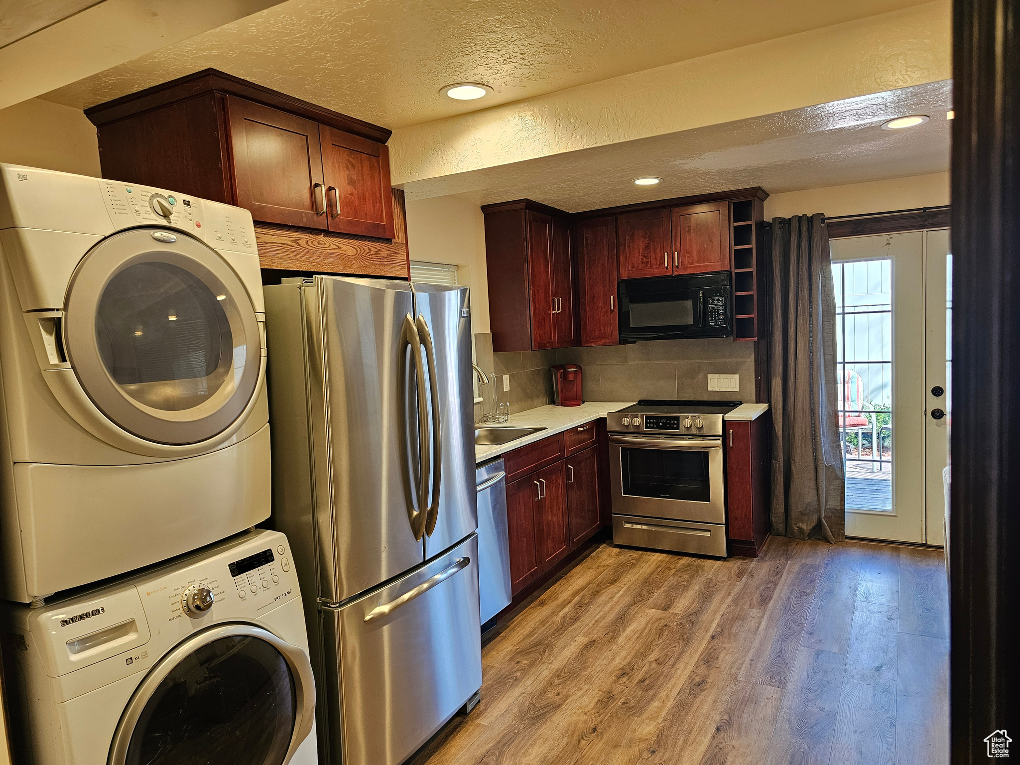 CASITA-Kitchen with stacked washer / drying machine, backsplash, stainless steel appliances, light hardwood / wood-style floors, and a textured ceiling