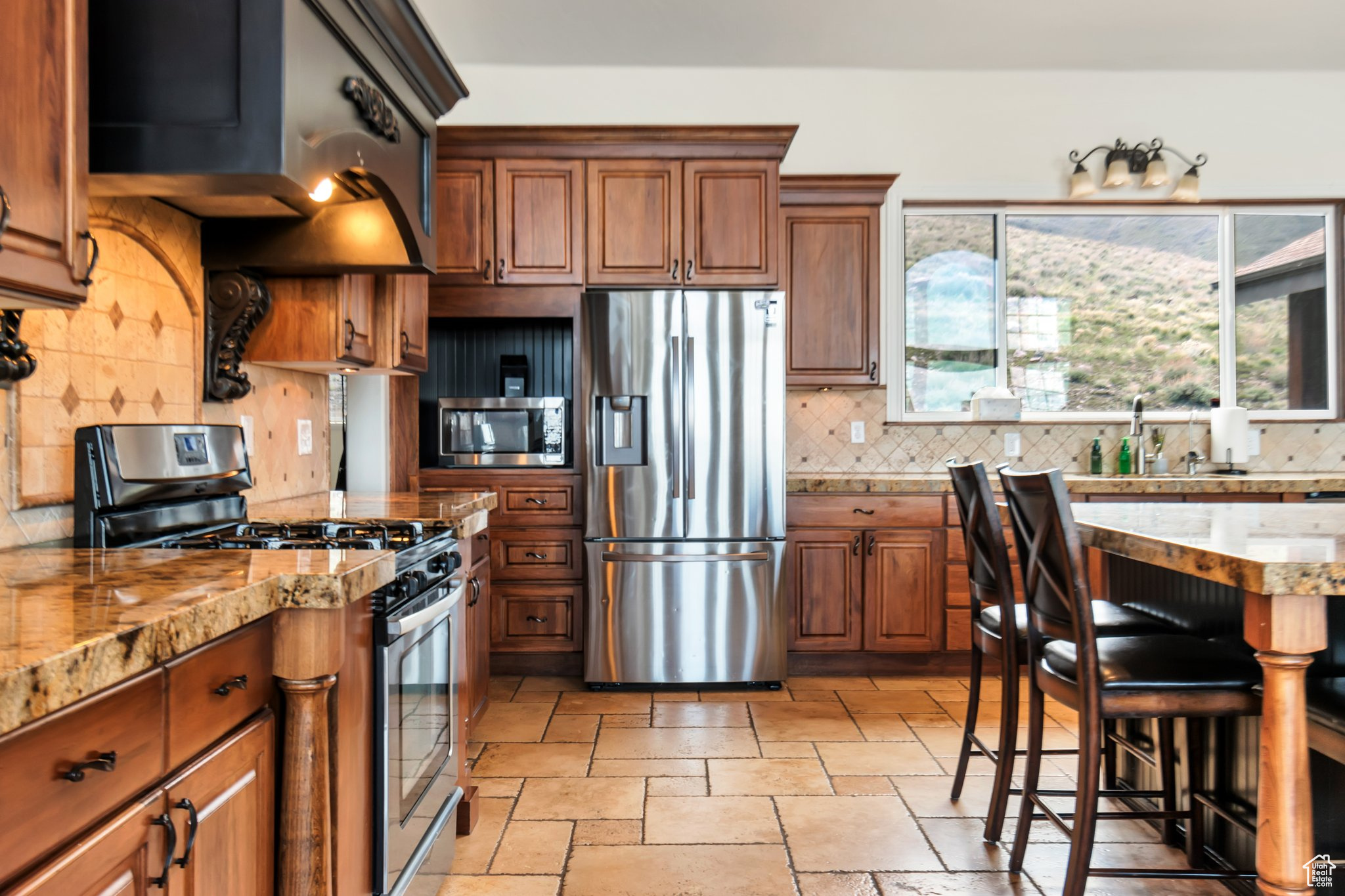 Kitchen with appliances with stainless steel finishes, sink, light tile flooring, backsplash, and a breakfast bar area