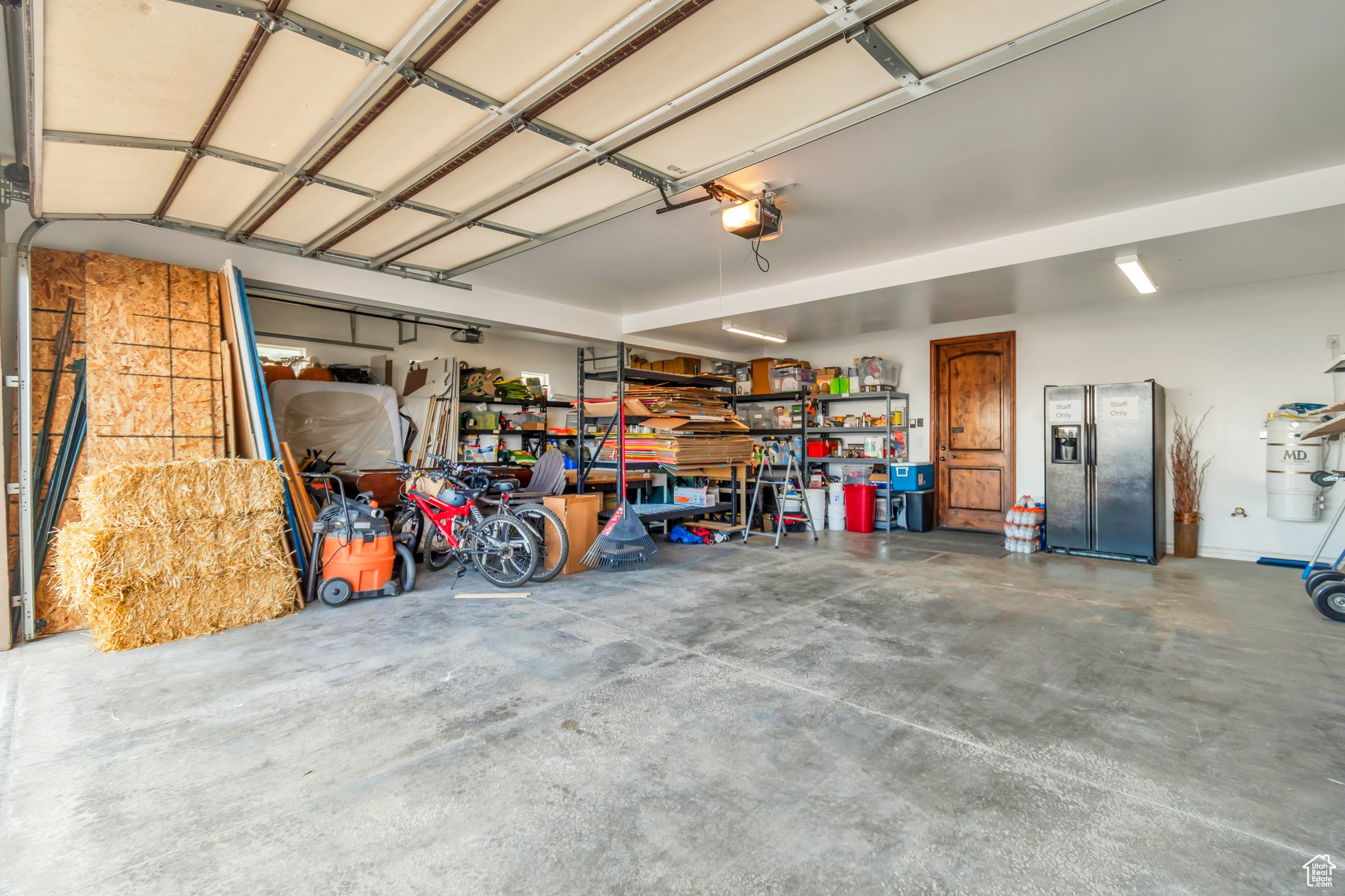 Garage featuring stainless steel fridge with ice dispenser, strapped water heater, and a garage door opener