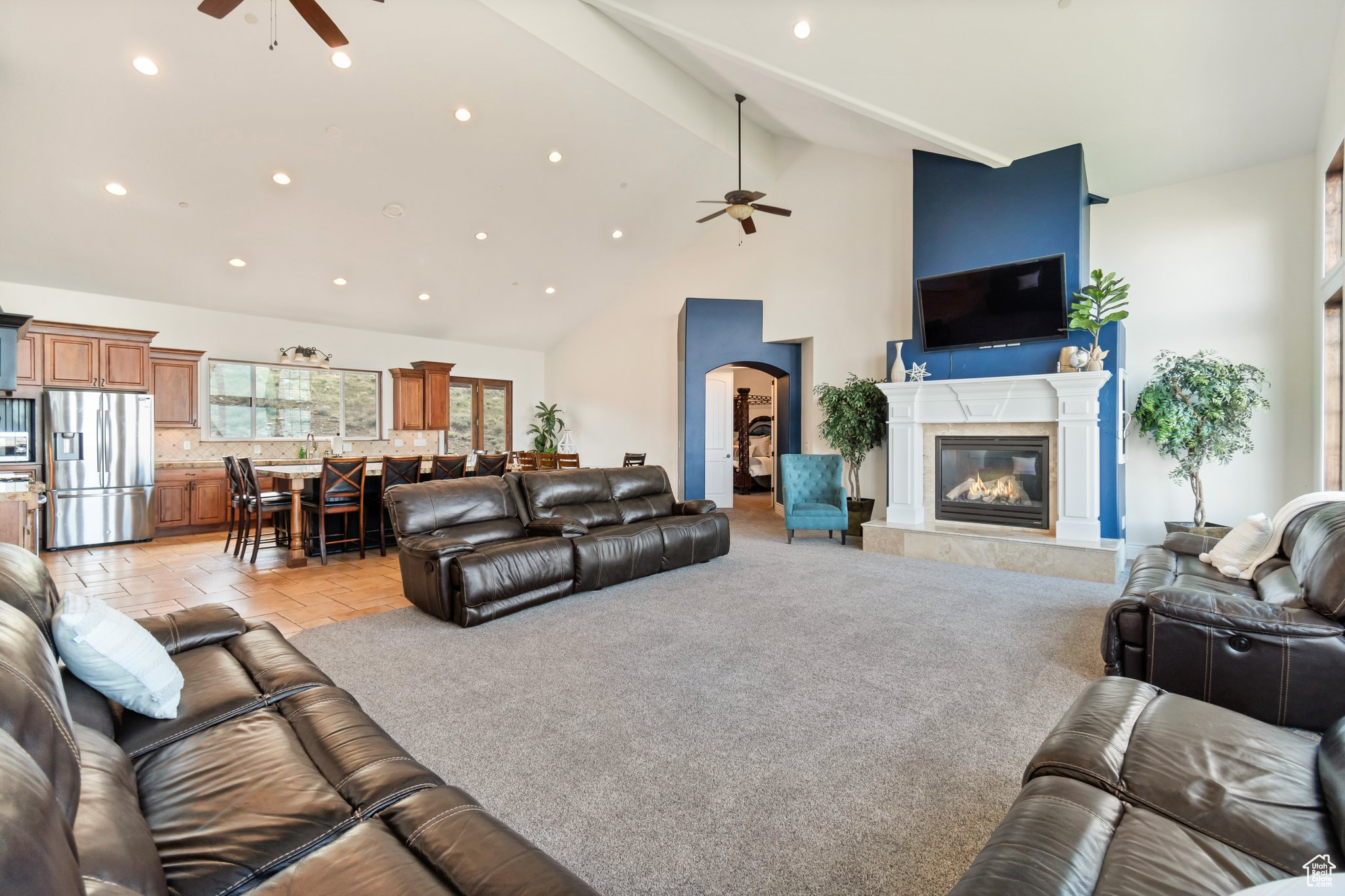 Carpeted living room with high vaulted ceiling, beamed ceiling, and ceiling fan