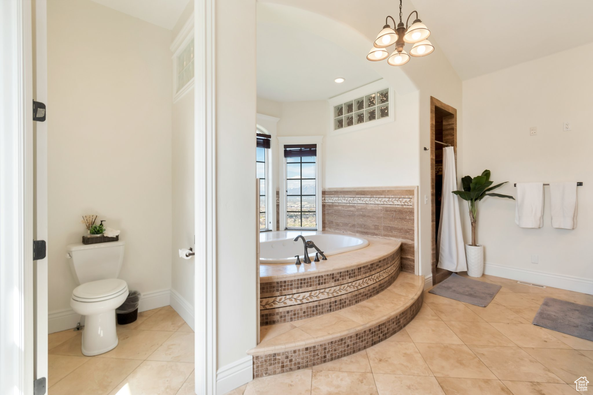 Bathroom featuring a notable chandelier, tile floors, toilet, and tiled tub