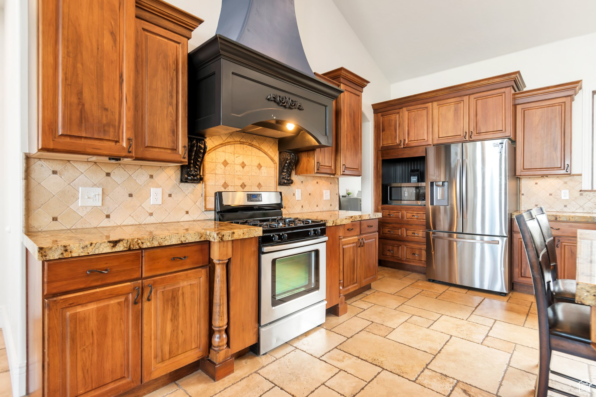 Kitchen featuring backsplash, stainless steel appliances, lofted ceiling, light stone counters, and light tile floors