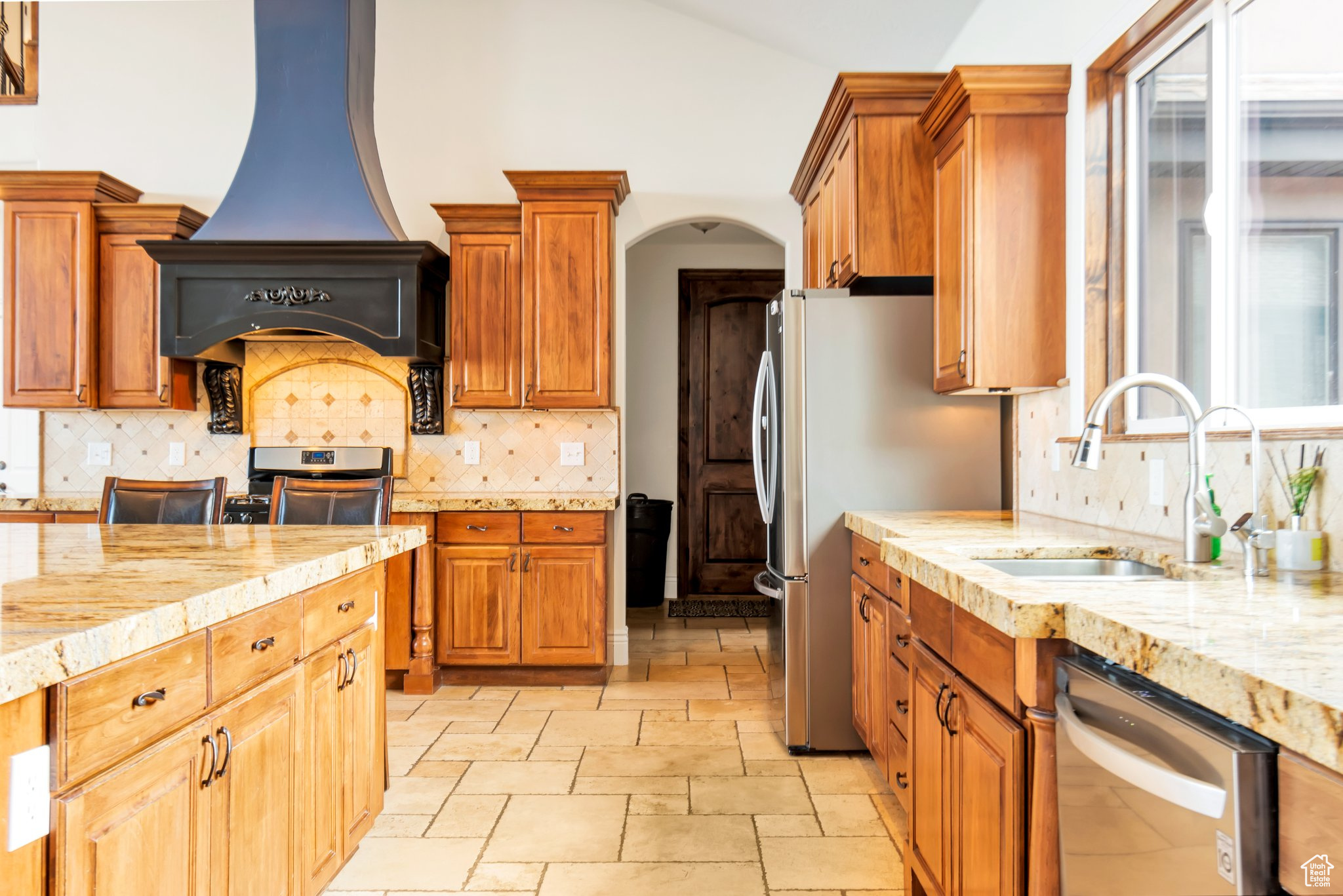 Kitchen featuring premium range hood, range, backsplash, light tile floors, and stainless steel dishwasher