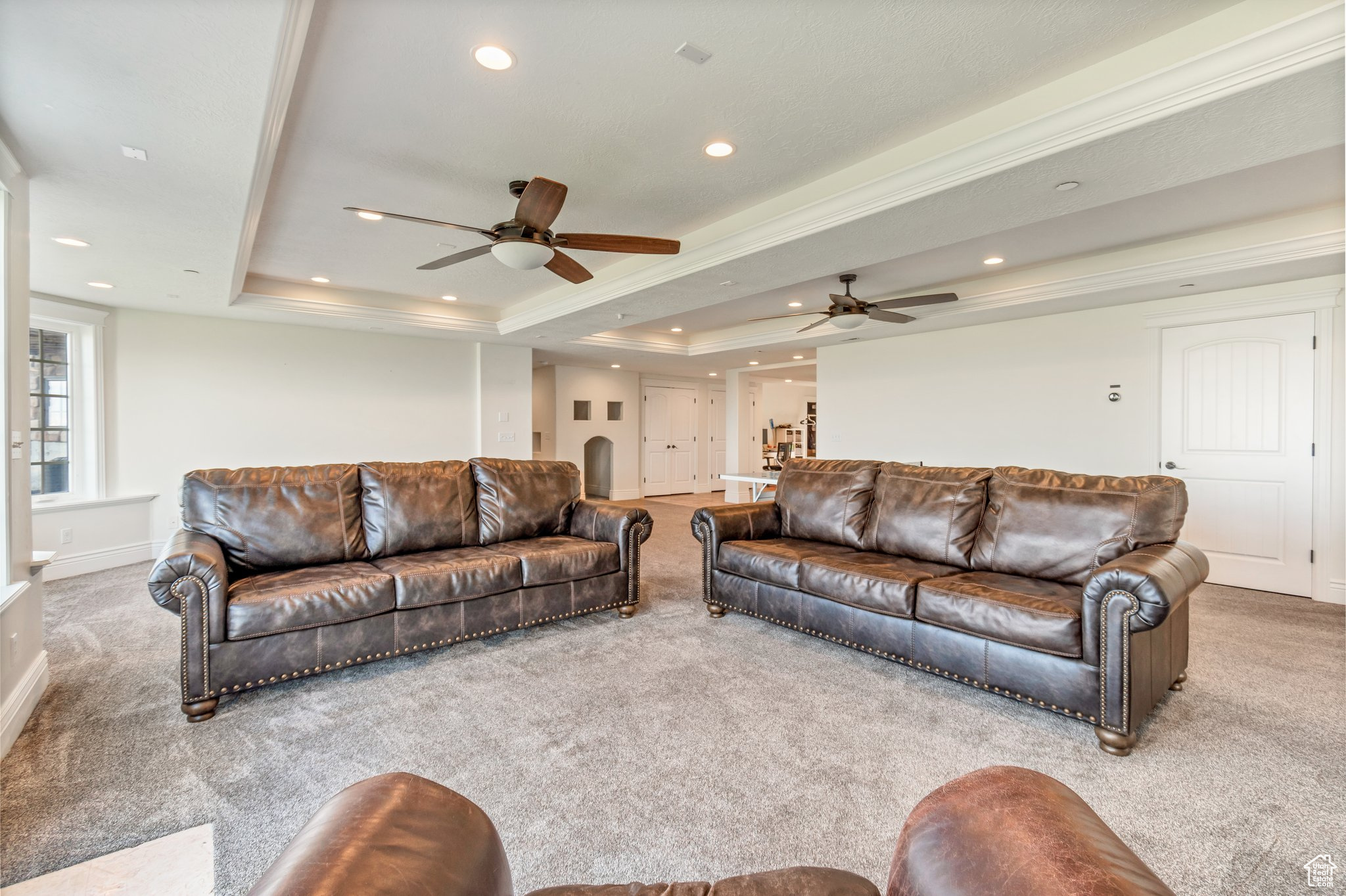 Living room with ceiling fan, carpet floors, and a tray ceiling