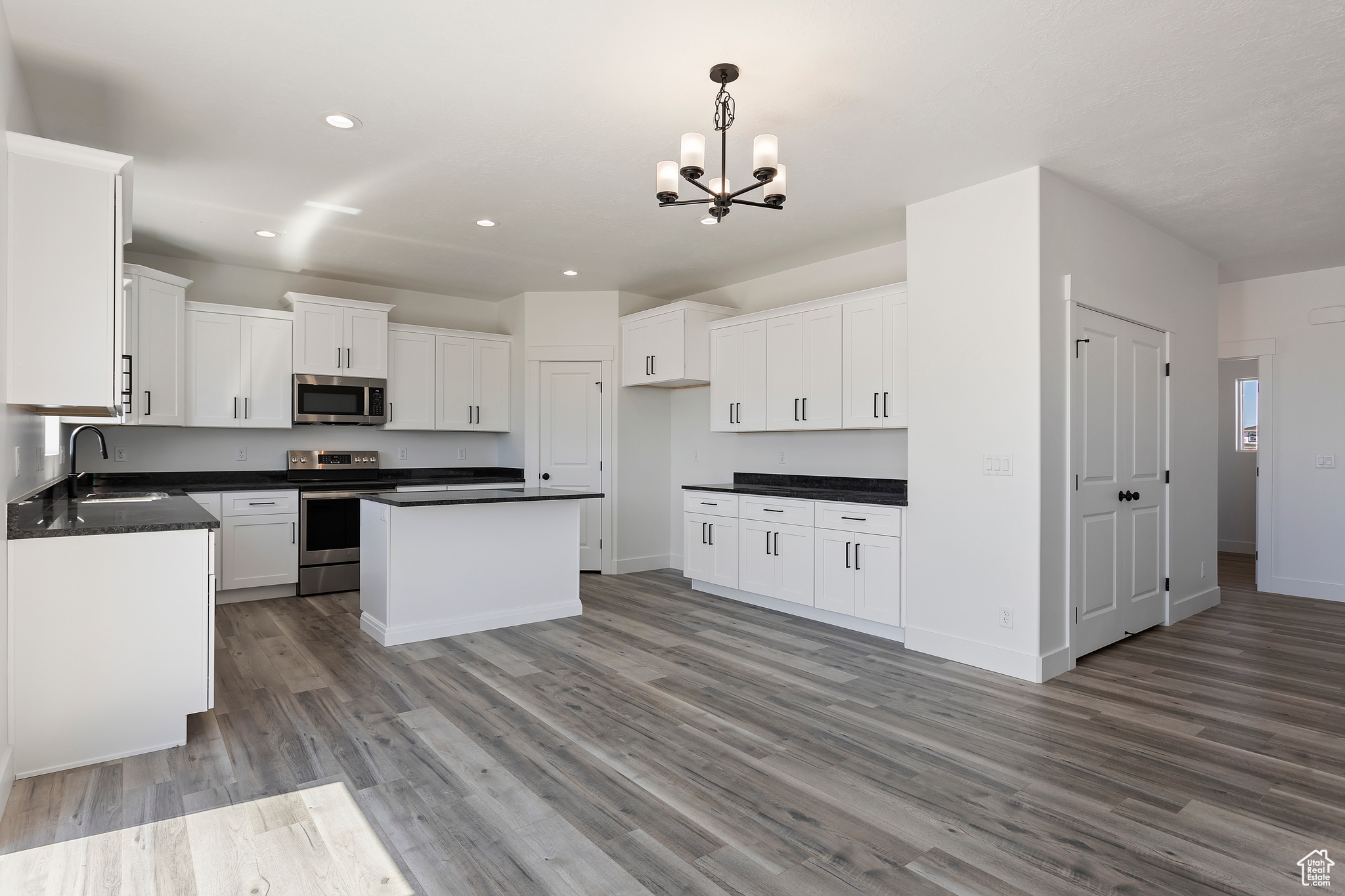 Kitchen with appliances with stainless steel finishes, white cabinets, sink, hanging light fixtures, and wood-type flooring