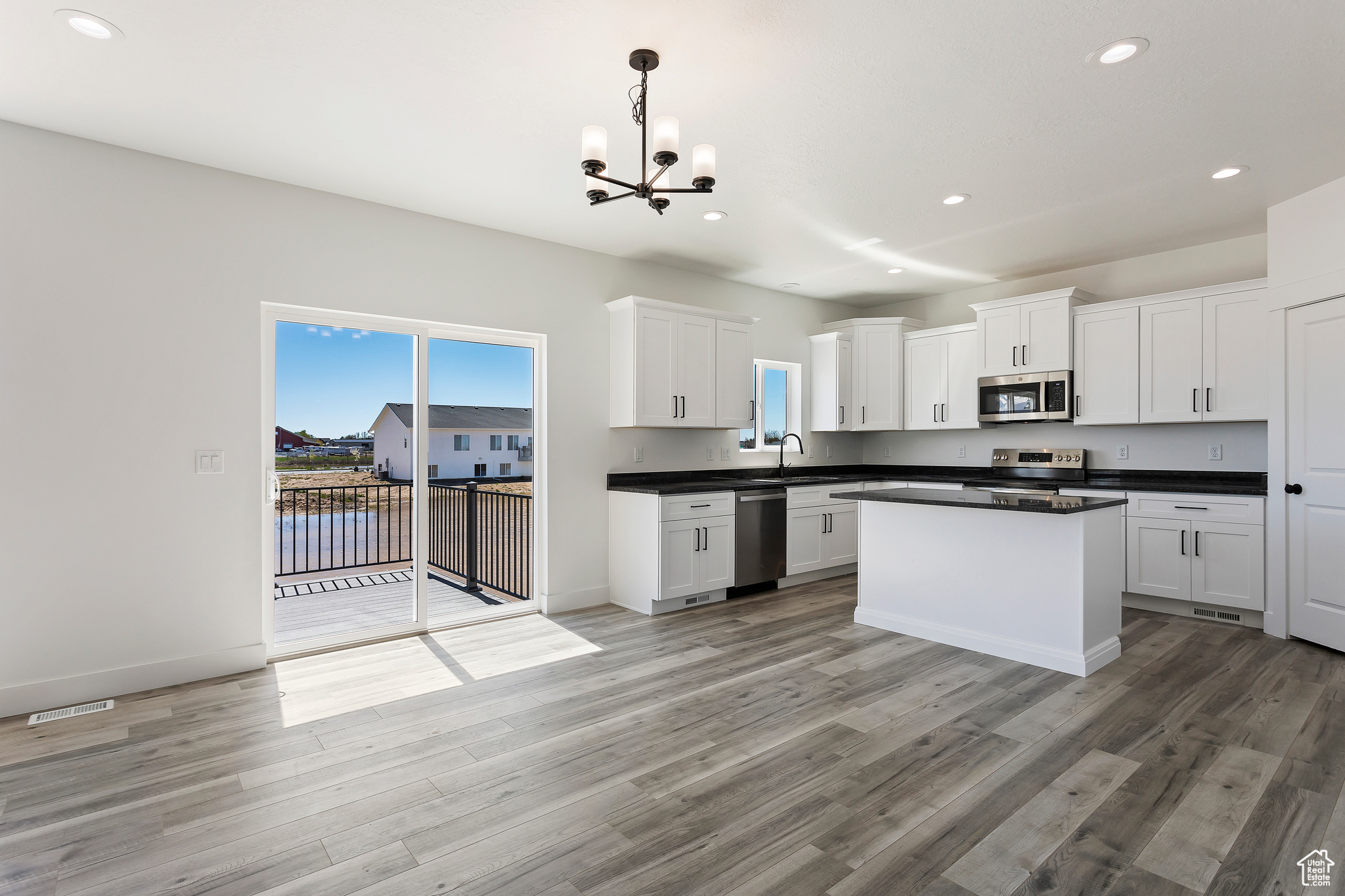 Kitchen featuring pendant lighting, appliances with stainless steel finishes, light hardwood / wood-style flooring, and white cabinets