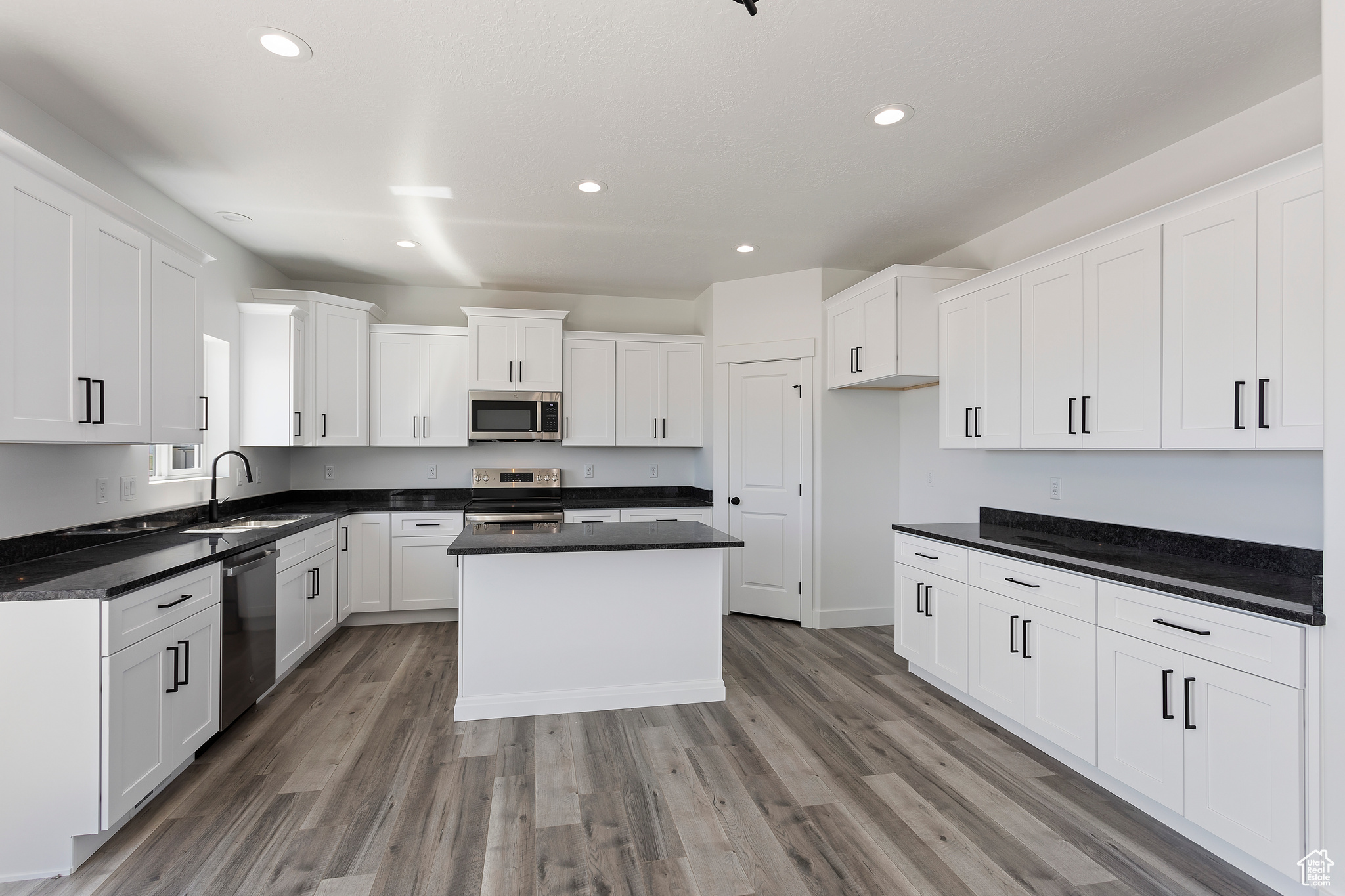 Kitchen featuring appliances with stainless steel finishes, a center island, sink, white cabinetry, and wood-type flooring