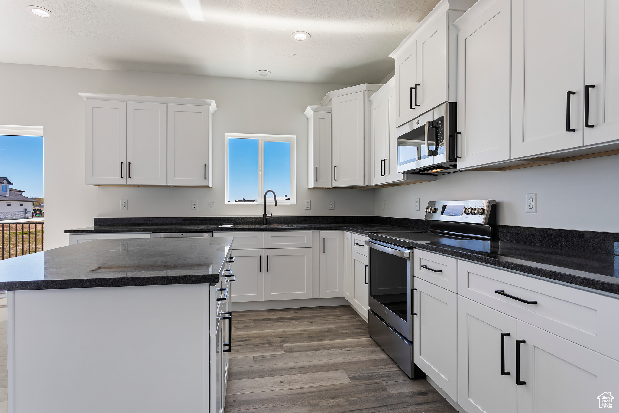 Kitchen featuring sink, stainless steel appliances, white cabinetry, hardwood / wood-style floors, and a center island