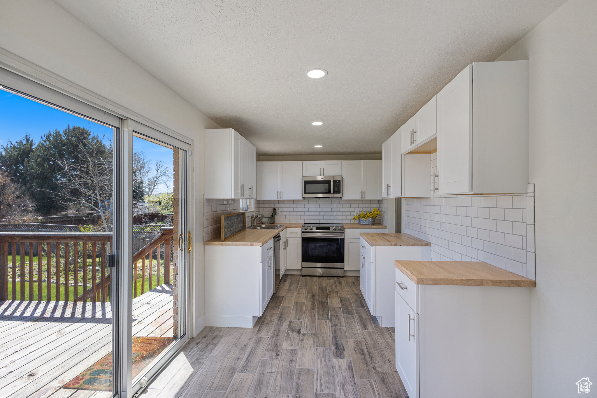Updated Kitchen featuring tiled backsplash, Stainless appliances , Butcher Block countertops, and tile floors.cabinetry, and wood counters. Sliding glass doors to large deck.
