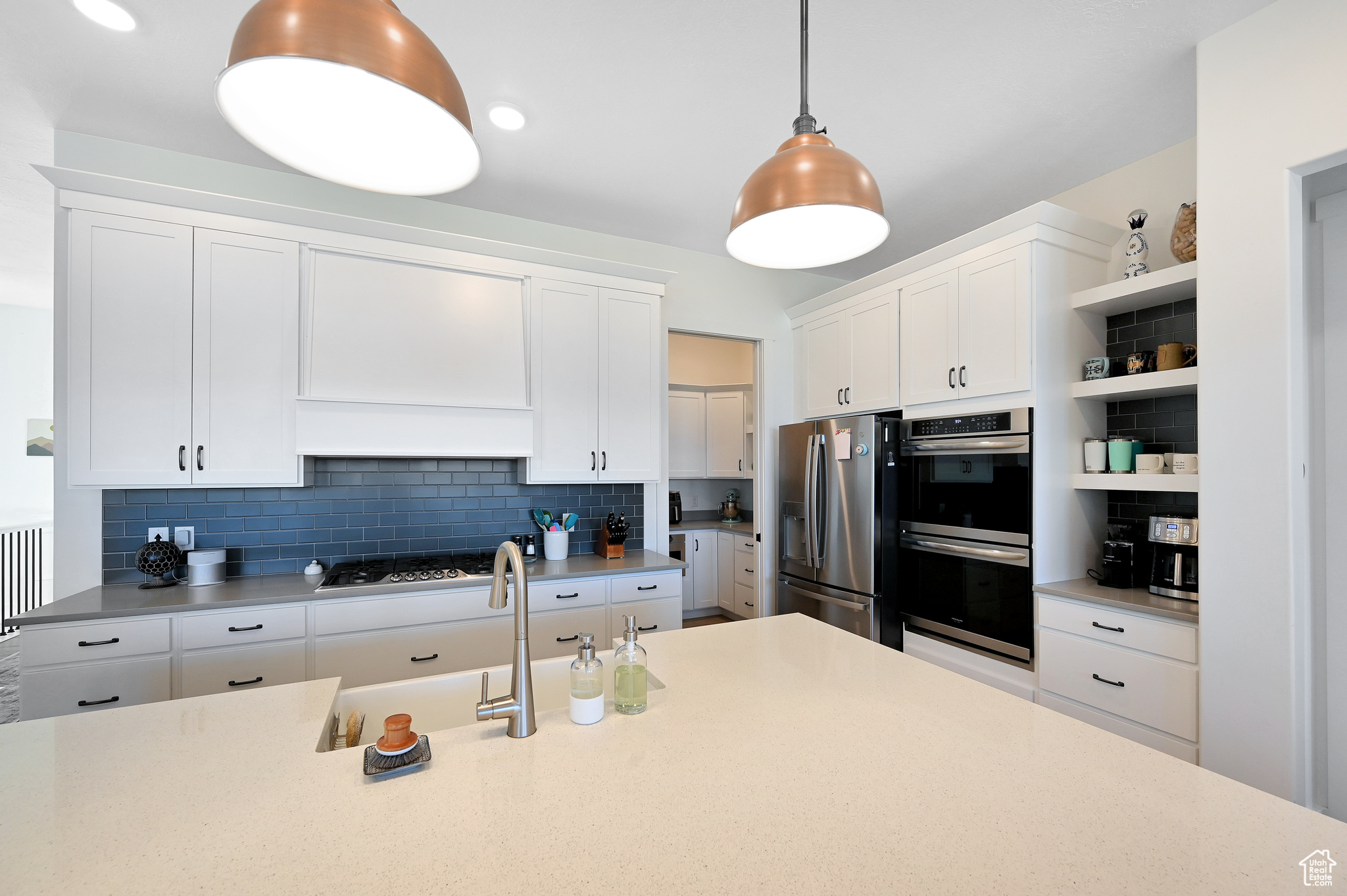 Kitchen with decorative light fixtures, backsplash, stainless steel appliances, white cabinetry, and sink