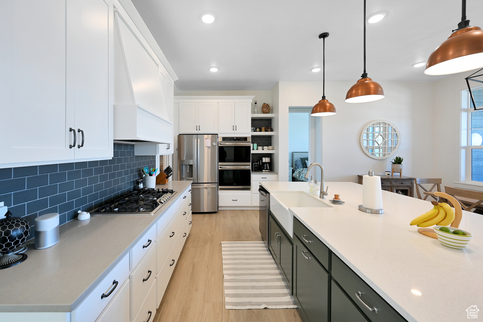 Kitchen featuring decorative light fixtures, backsplash, stainless steel appliances, light hardwood / wood-style floors, and white cabinets