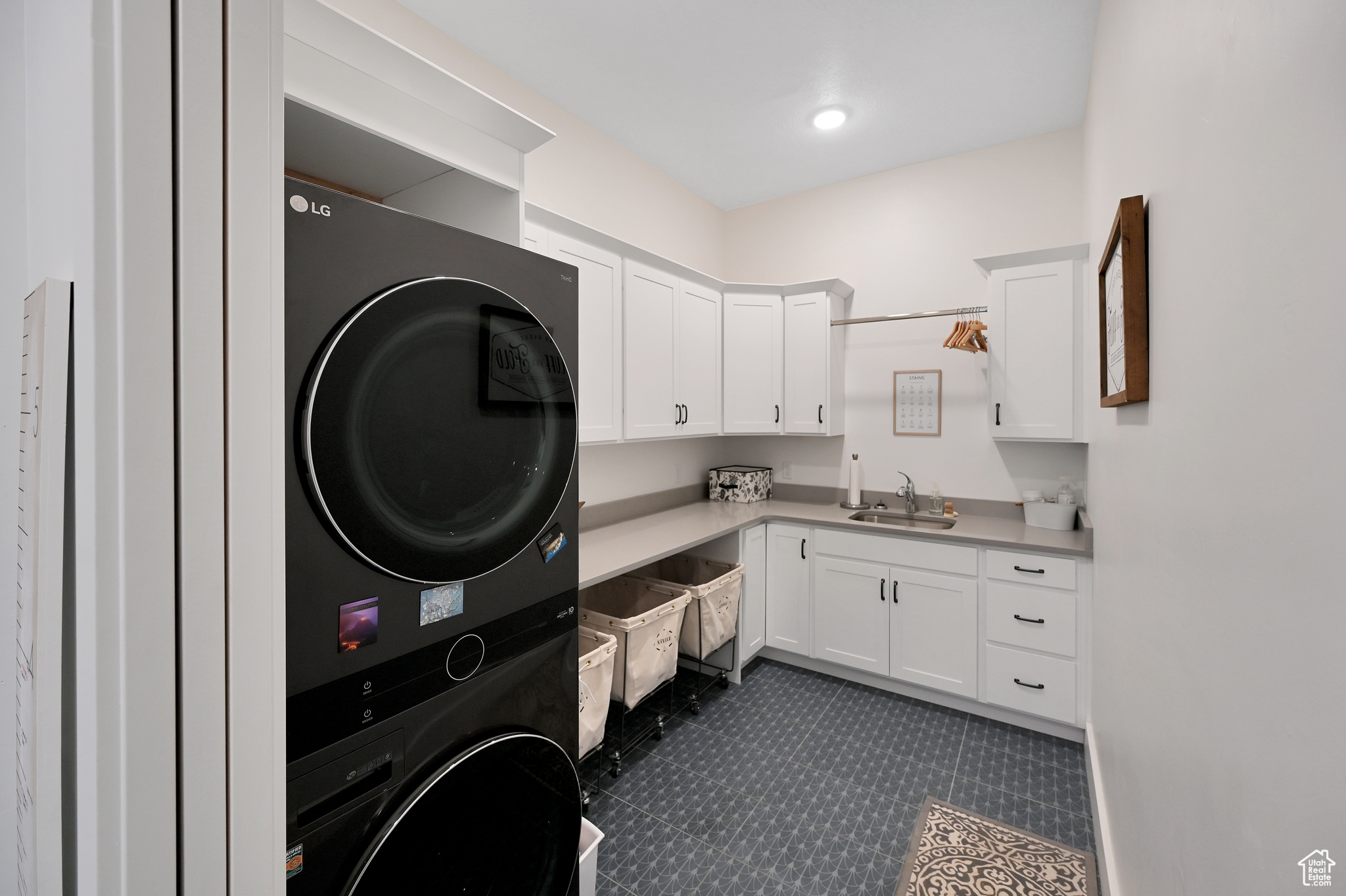 Clothes washing area with cabinets, stacked washer and clothes dryer, sink, and dark tile floors