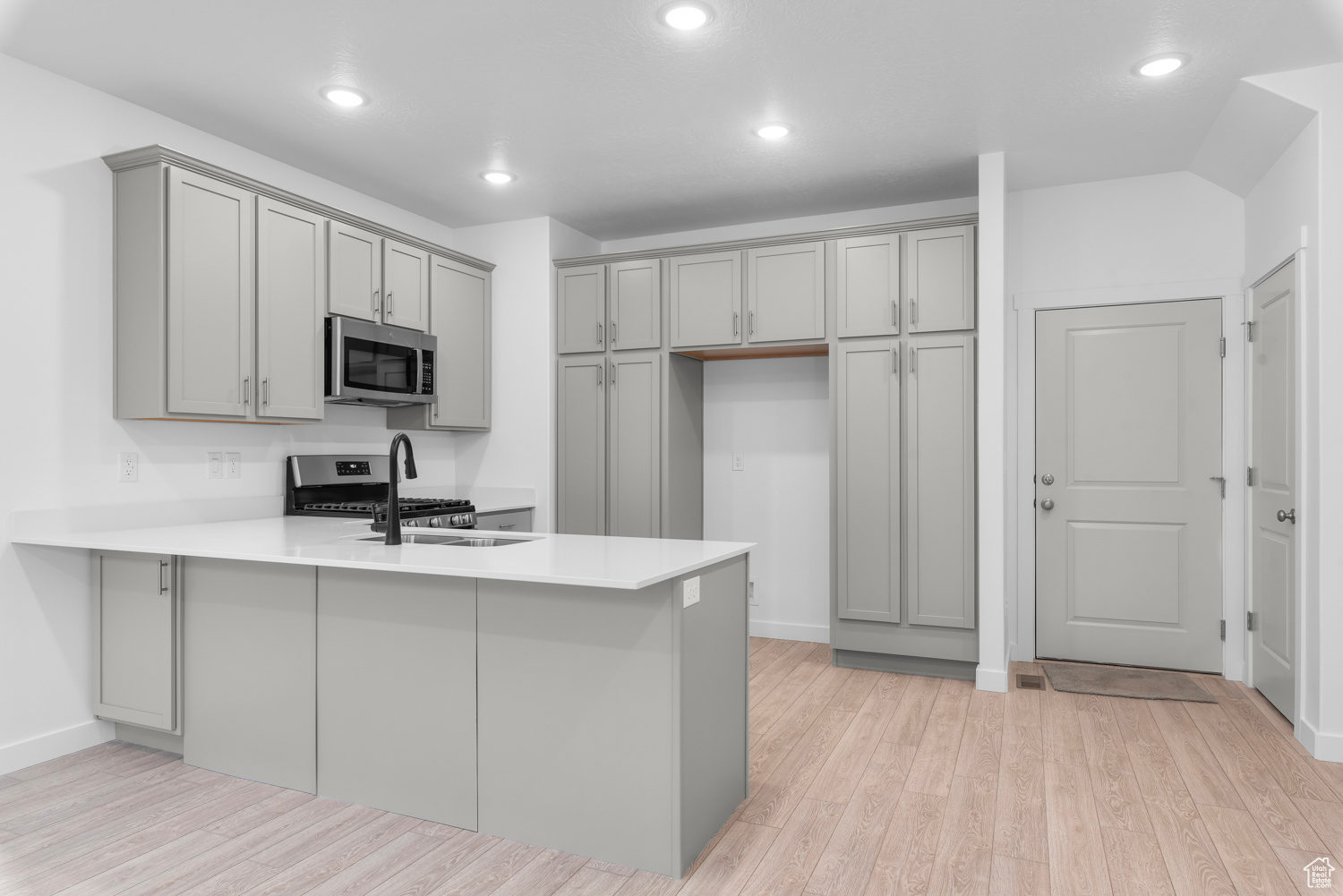 Kitchen featuring gray cabinets, stainless steel appliances, light hardwood / wood-style floors, and kitchen peninsula